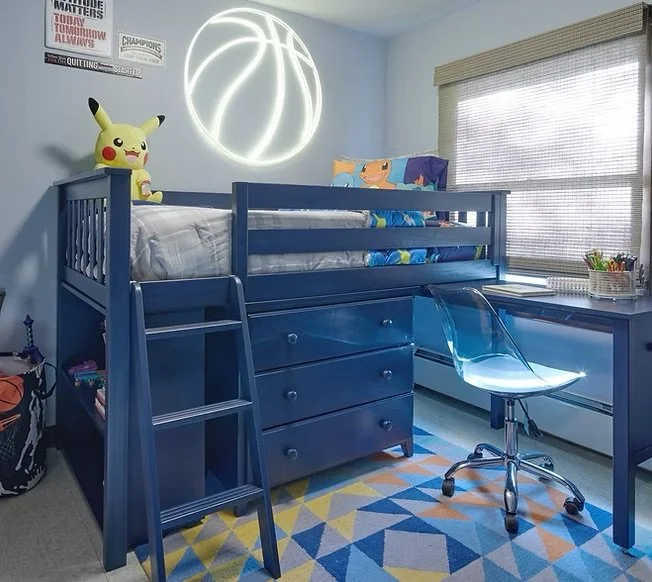 A bedroom with a blue bunk bed featuring a Pikachu plush toy on top, a neon basketball light on the wall, and a desk with a transparent chair and a window with blinds.