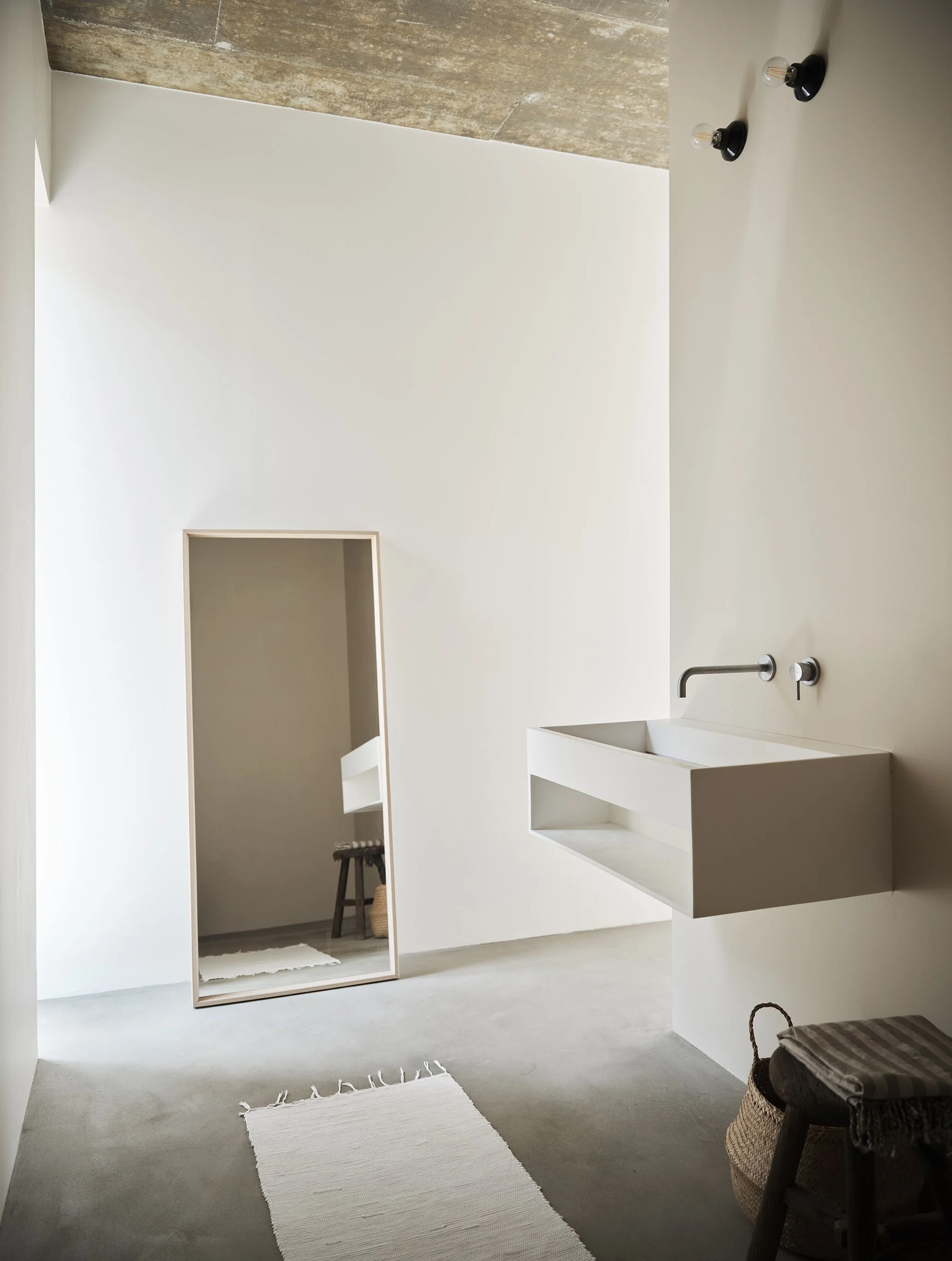 Person pouring a drink at a table with sliced bread, toasted bread, a glass of rosé wine, glasses of water, a white textured vase with pink flowers, and a dark tumbler. Silverware on a napkin on a gray table surface.