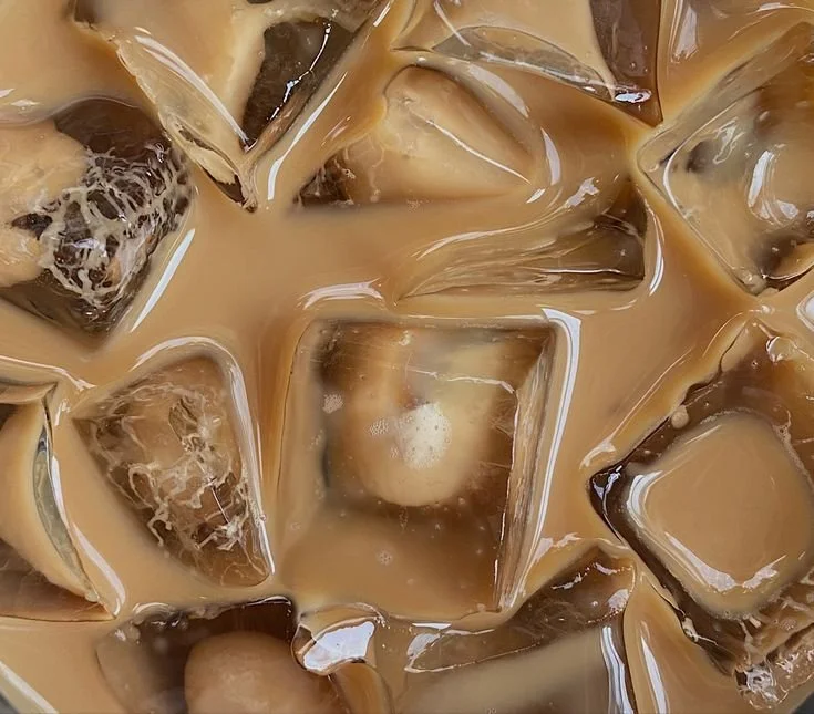Close-up of iced coffee with milk, showing ice cubes and swirls of coffee and cream.