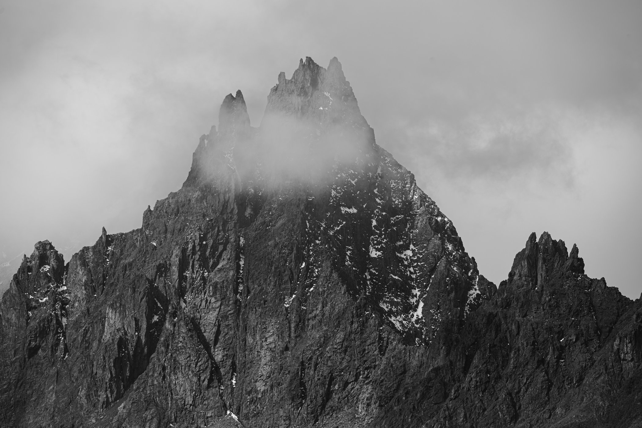 Montagne rocheuse enneigée sous un ciel nuageux avec un peu de brume autour de la cime.