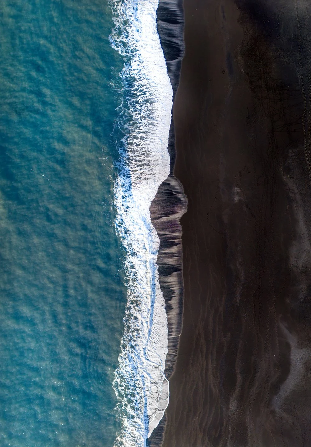 Vague de mer s'écrasant sur une plage de sable noir en Islande, vue de haut.
