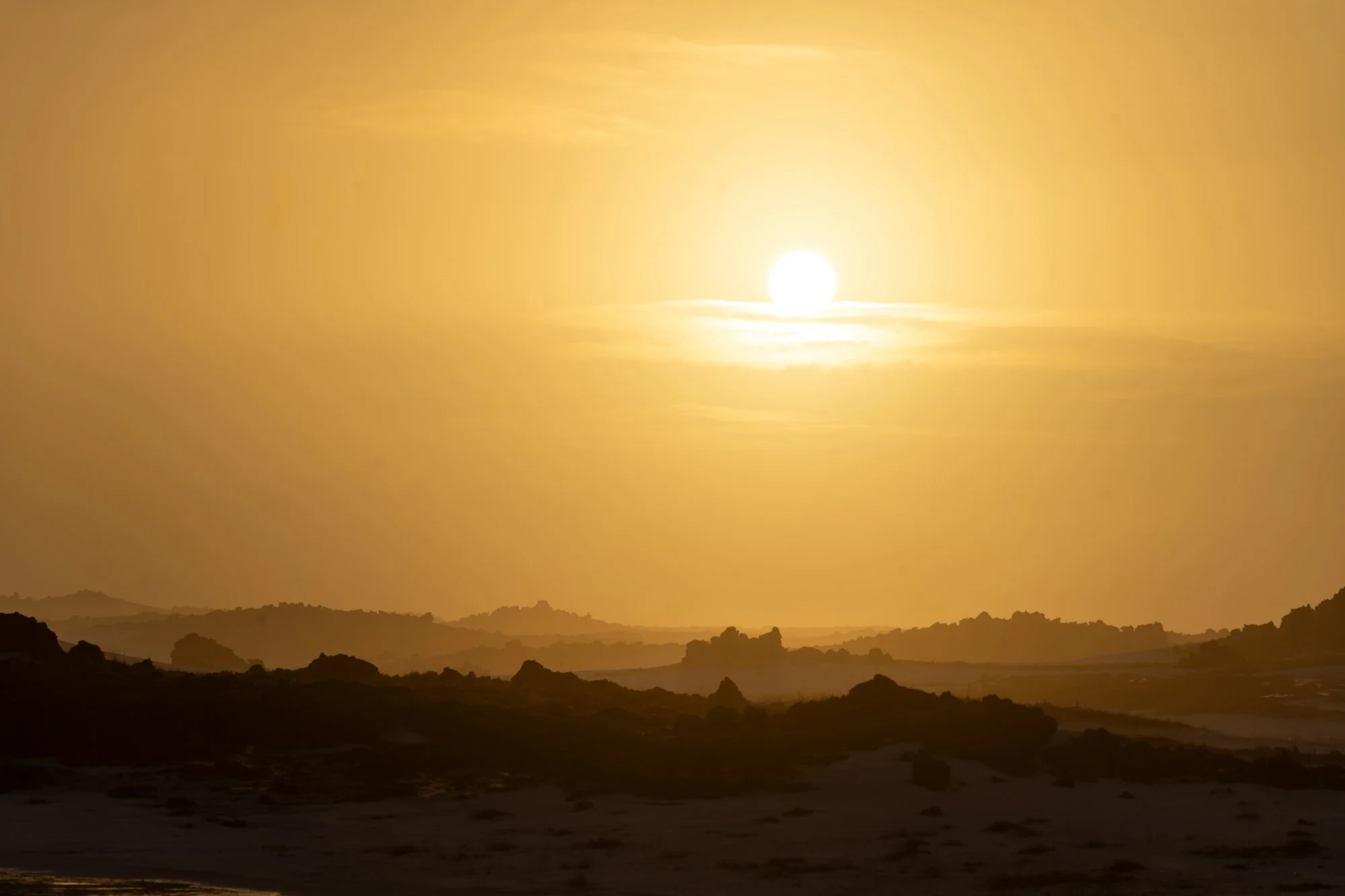 Un paysage désertique avec des collines sombres sous un ciel jaune avec un soleil brillant.