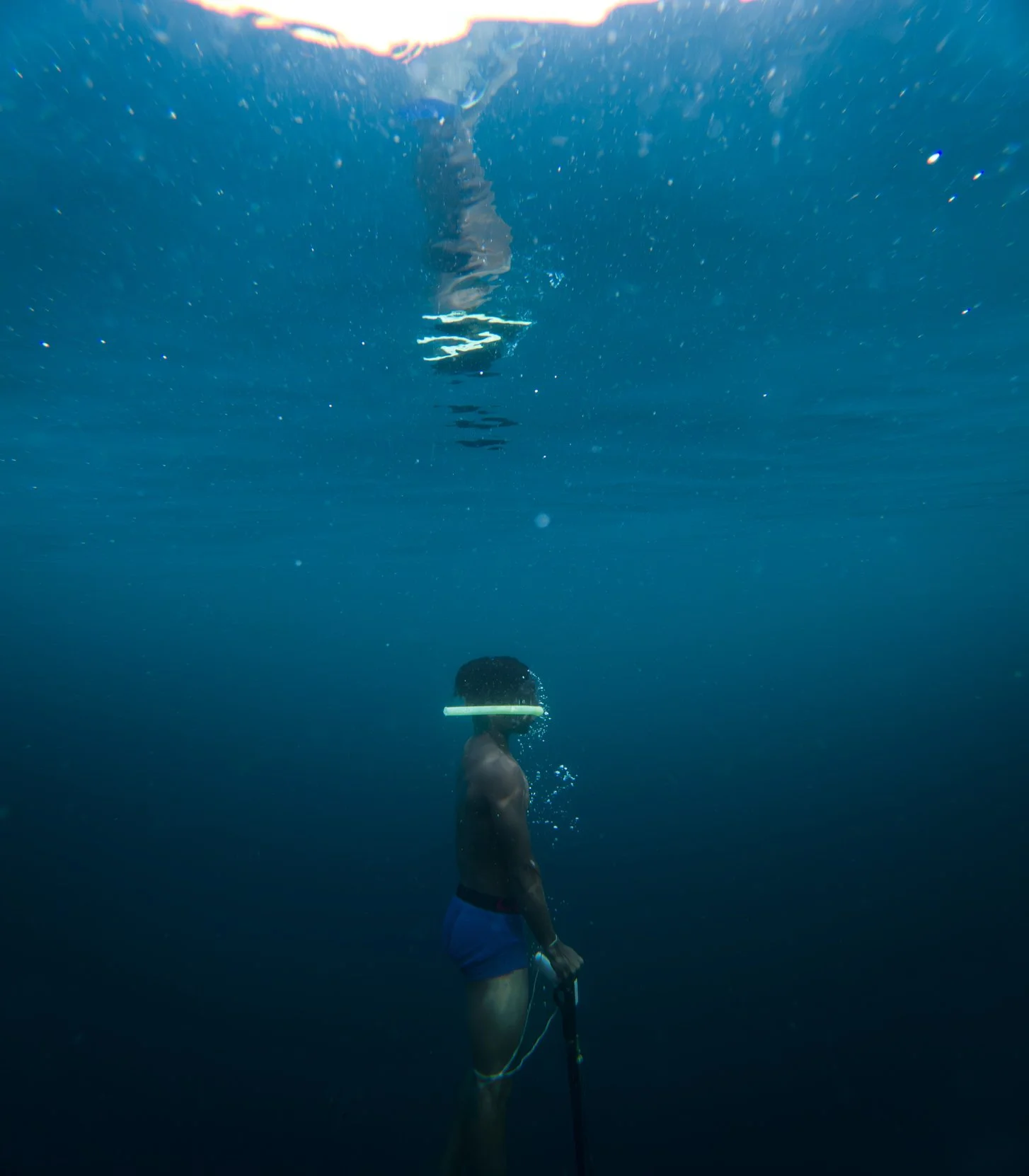 Un garçon nageur en train de remonter à la surface de l'eau, avec une bulle d'air en anneau autour de son visage. L'image capture une scène sous-marine.