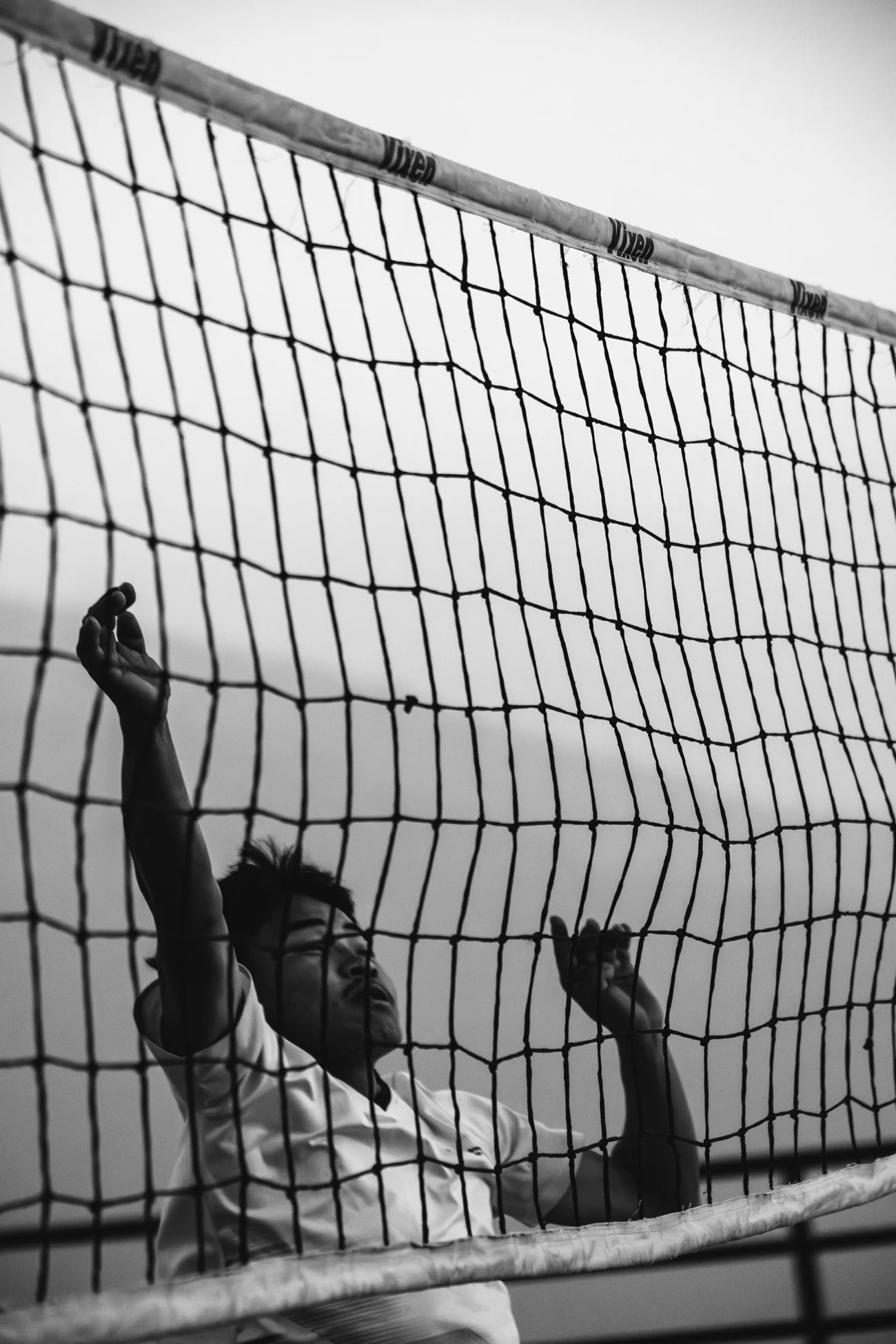 Un joueur de volley-ball avec une expression concentrée, vu à travers le filet, en action lors d'un match.