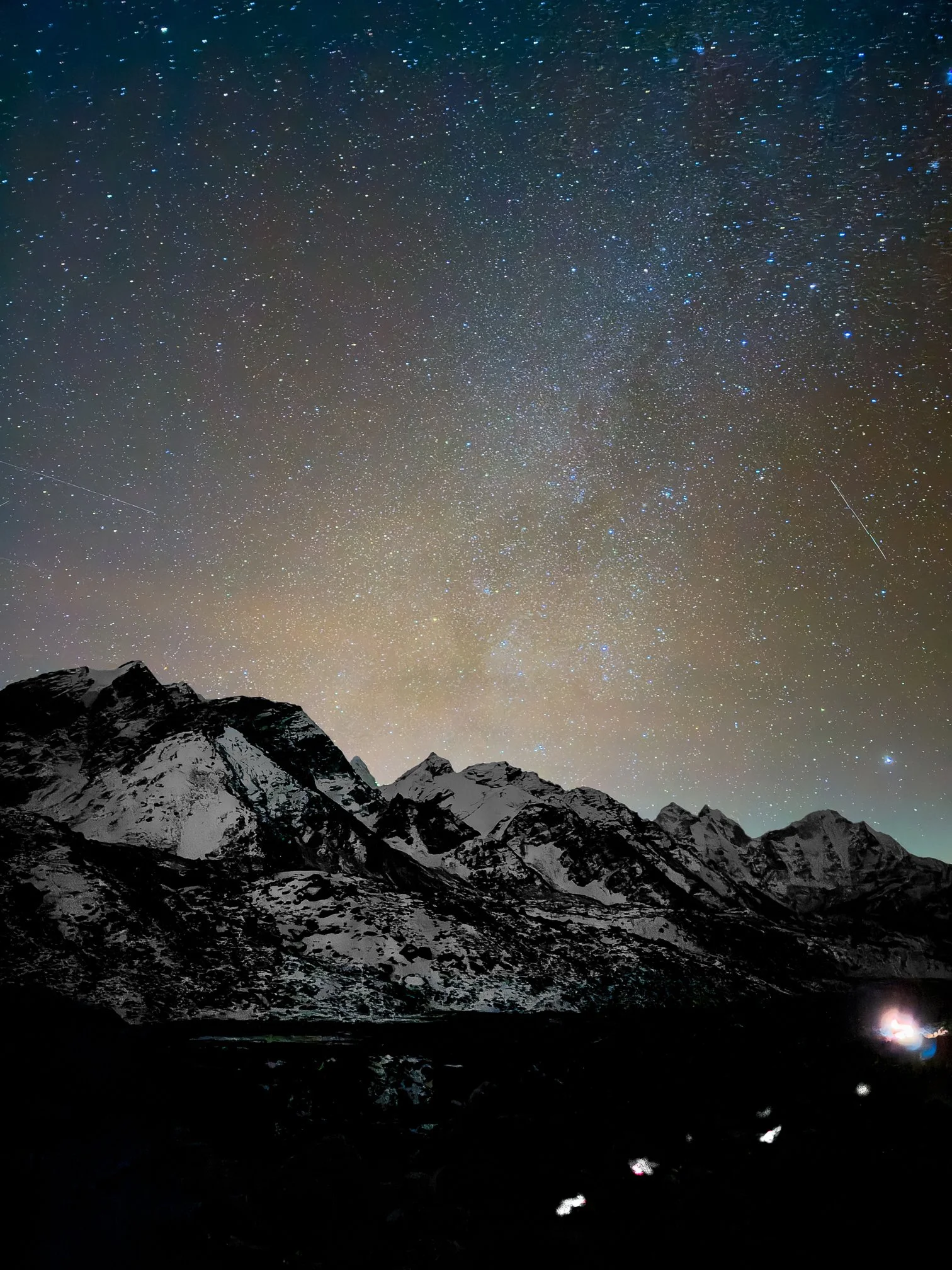 Ciel étoilé au-dessus de montagnes enneigées dans une région isolée, avec quelques étoiles filantes visibles.