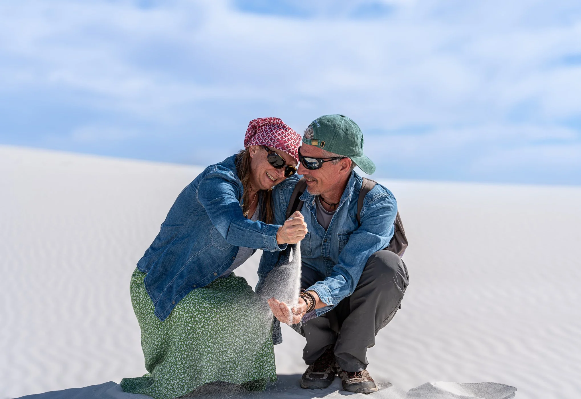 Un couple souriant dans un paysage de désert de sel, ils tiennent un peu de sel dans leurs mains, portant des vêtements décontractés avec des chapeaux et des lunettes de soleil.