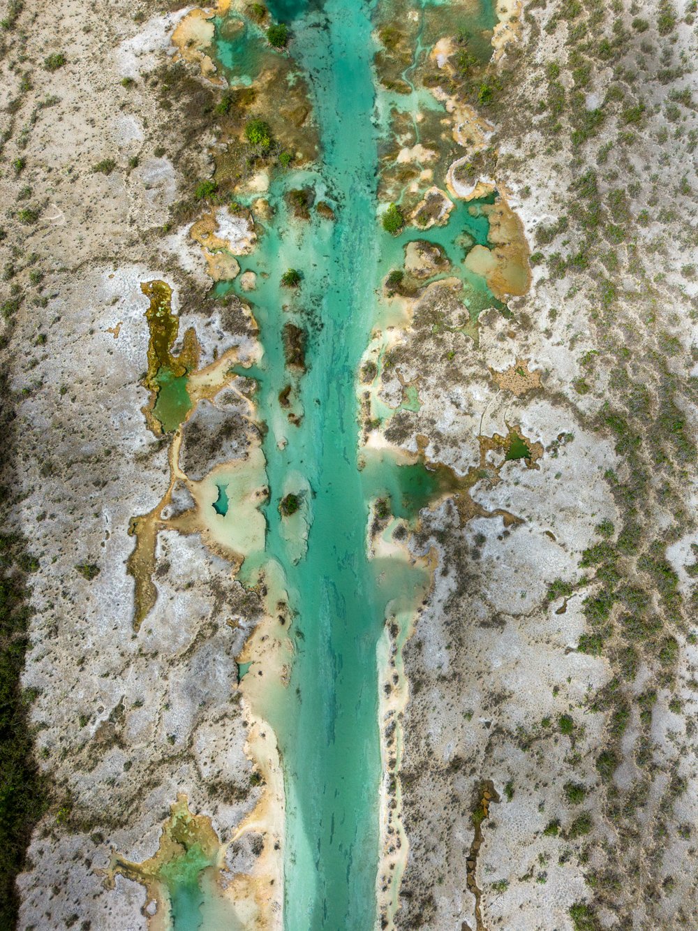Photo aérienne d'un lac turquoise avec plusieurs petites îles et zones humides entouré d'un terrain aride avec peu de végétation.