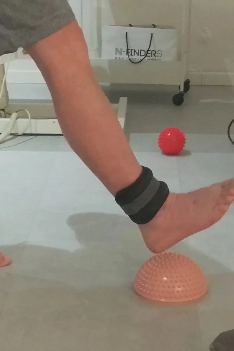 Person walking barefoot over textured balance equipment with ankle weights in an indoor space.