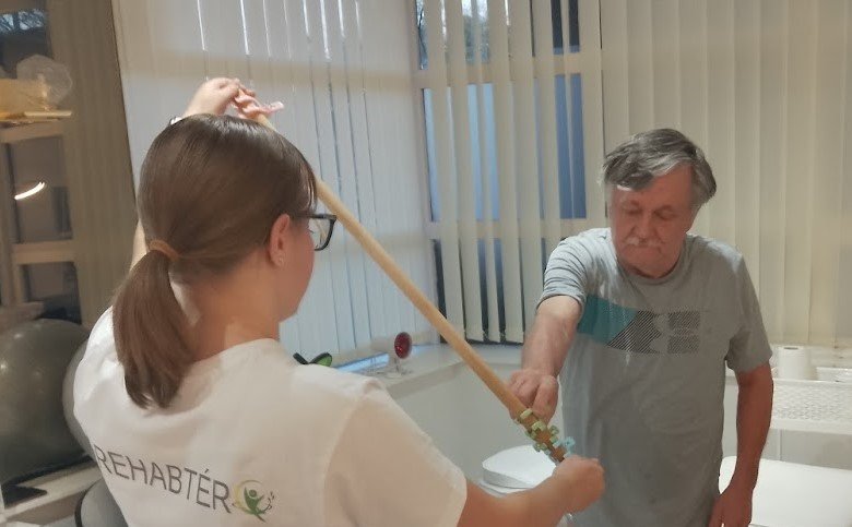 A young woman assisting an elderly man with a mobility aid during a therapy session.