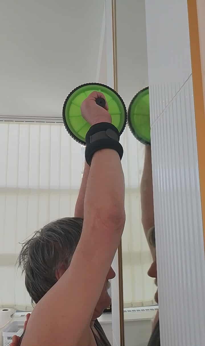 A person using a green and black handheld mirror in front of a mirror to apply makeup or groom their face, with their arm raised and their reflection visible.