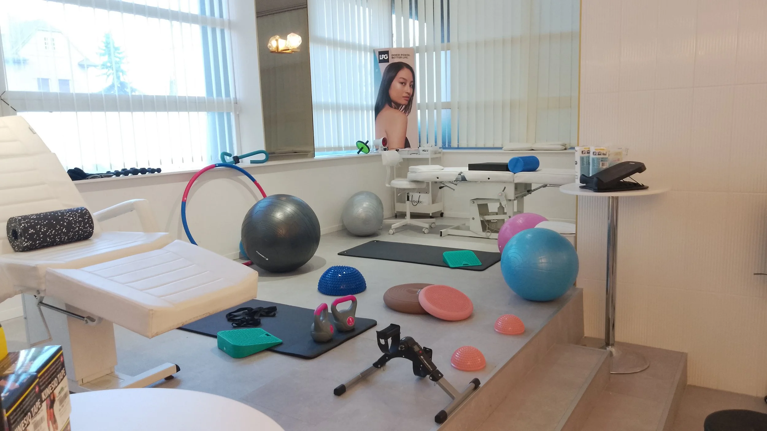 Therapy or physical rehabilitation room with various exercise balls, weights, balance equipment, an examination table, and a promotional poster of a woman with long hair.