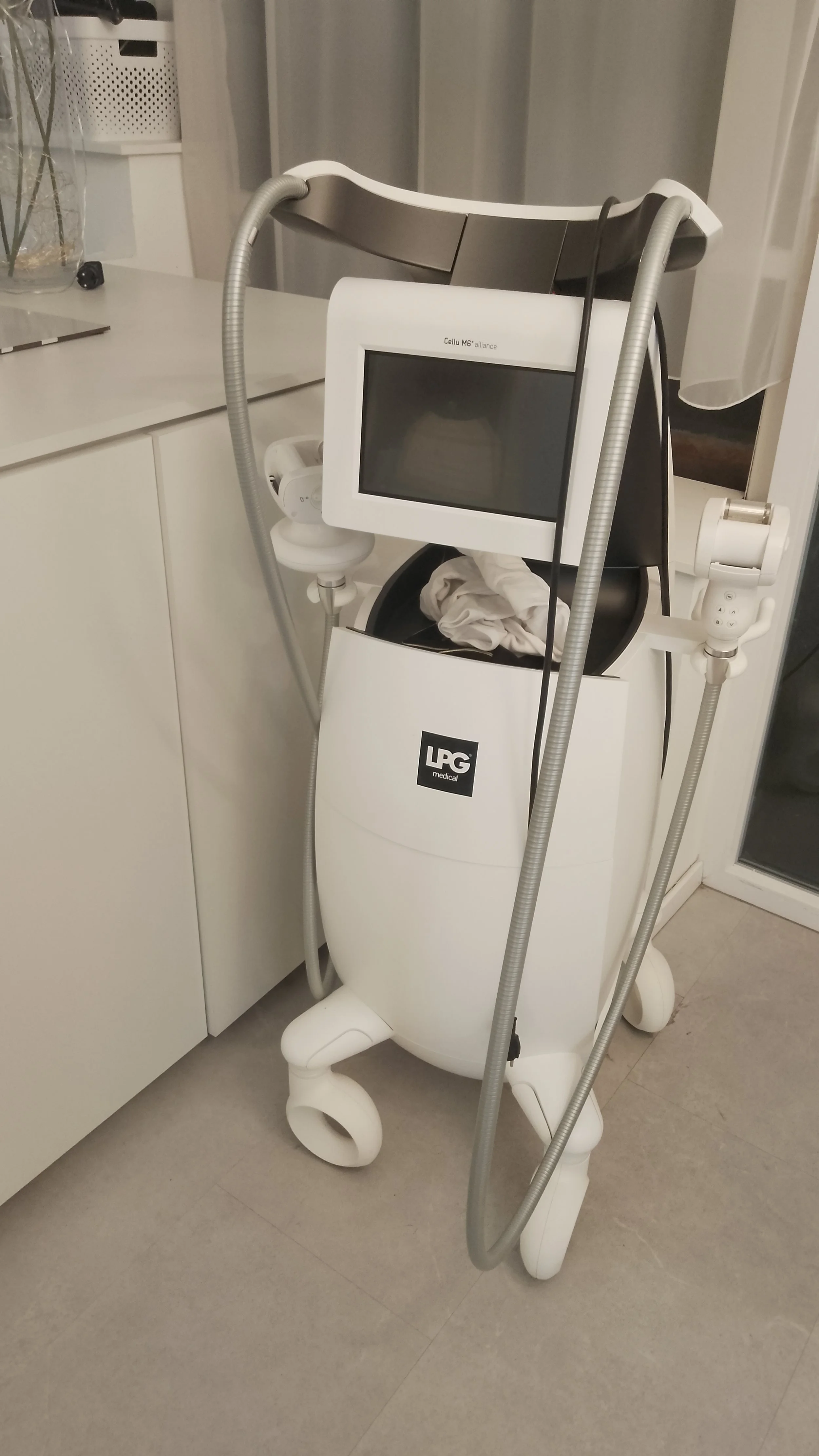 Medical device with a screen and hoses, labeled 'LPG medical', placed next to a white cabinet and curtains.
