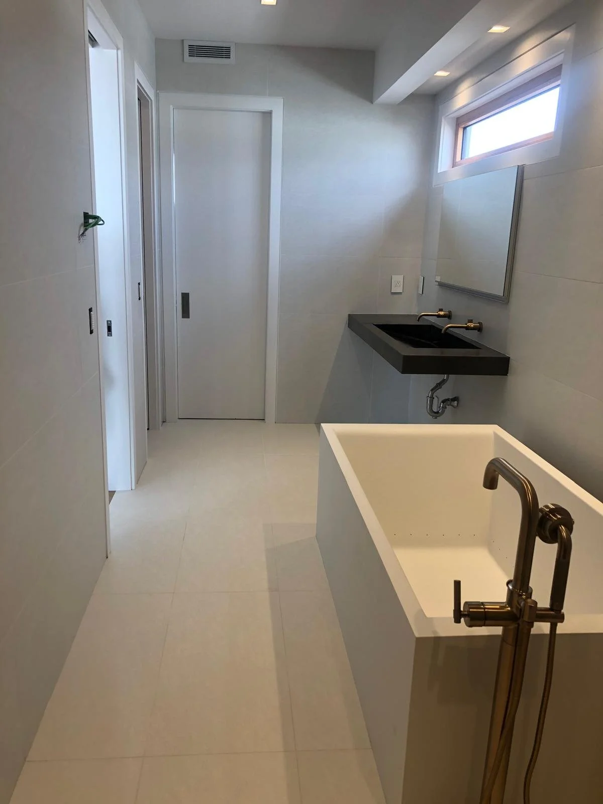 A modern bathroom with a white bathtub, black sink with gold fixtures, and a window near the ceiling.