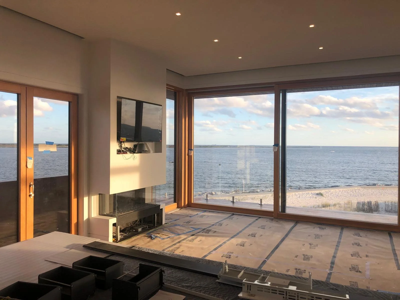Living room with large windows overlooking the ocean, with a partial view of a wall-mounted television and a fireplace.