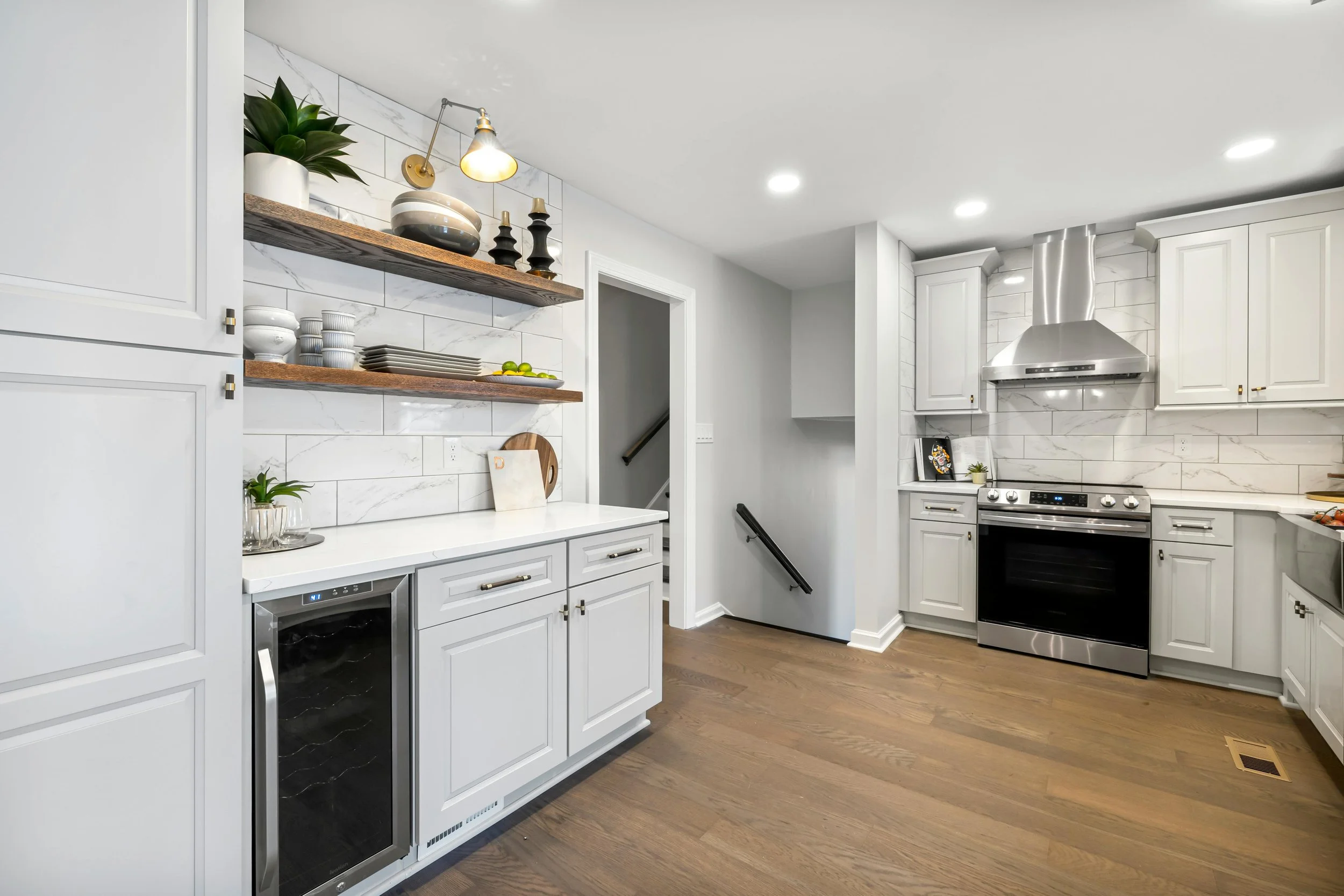 Modern kitchen with white cabinets, stainless steel stove, wood flooring, and open floating shelves holding dishes, plants, and decor.