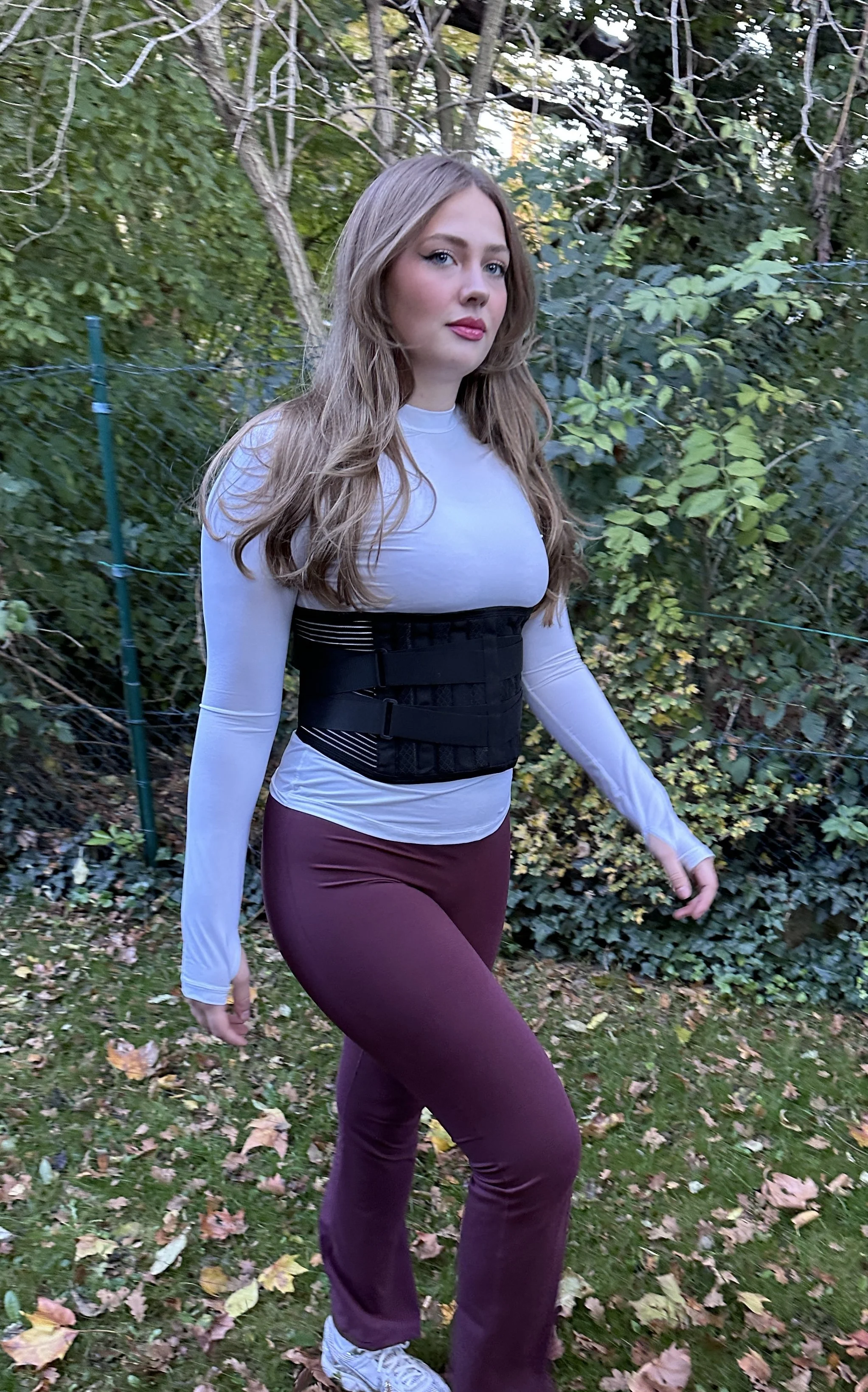 Junge Frau im Garten mit bunter Kleidung, lange Haare, aber keine besonderen Merkmale sichtbar.