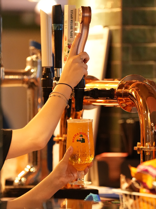 Person pouring beer from tap into a glass at a bar.