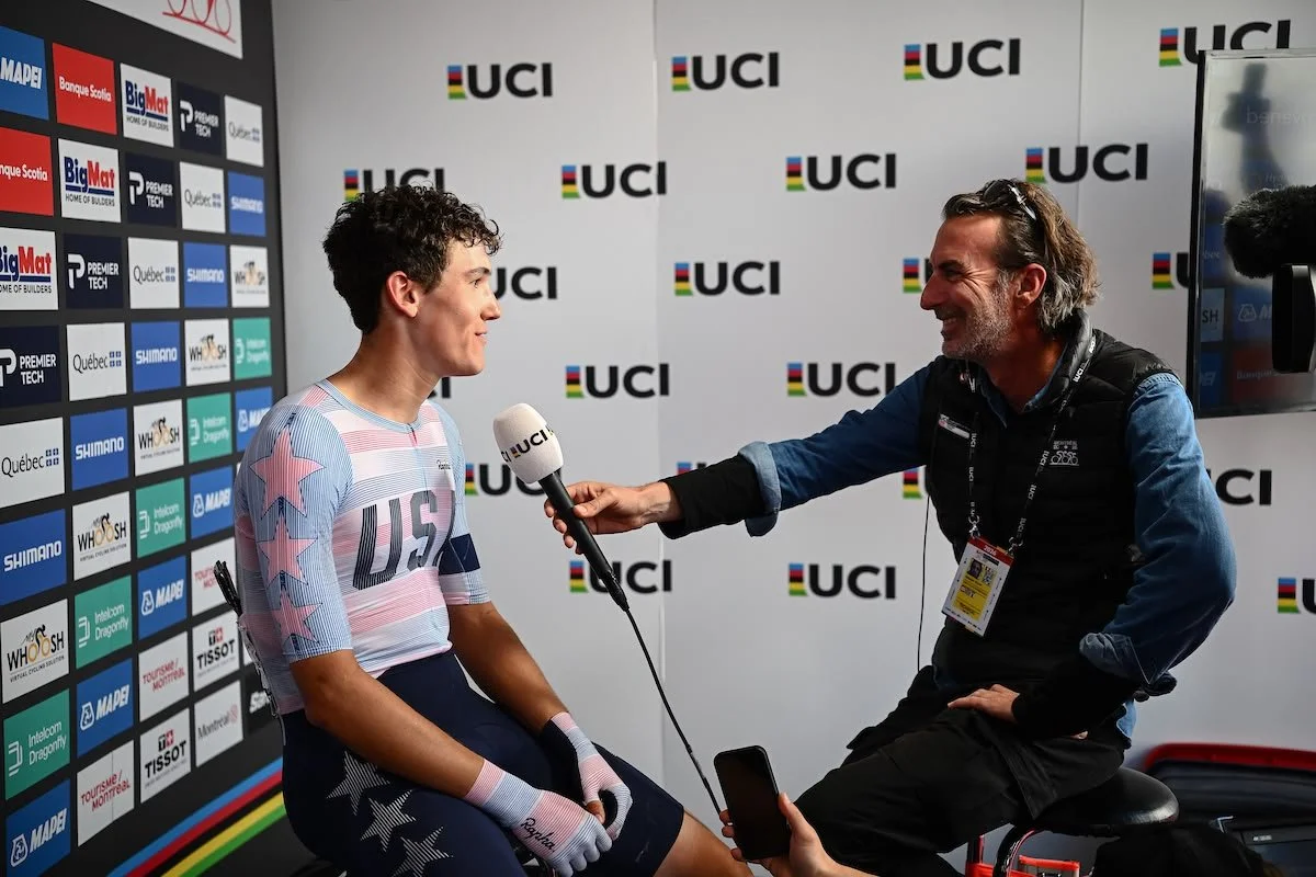 Ashlin Barry being interviewed wearing at the UCI  U23 World Cycling championships, USA cycling jersey. The background has UCI logos and sponsor banners, indicating a sports event or press conference.