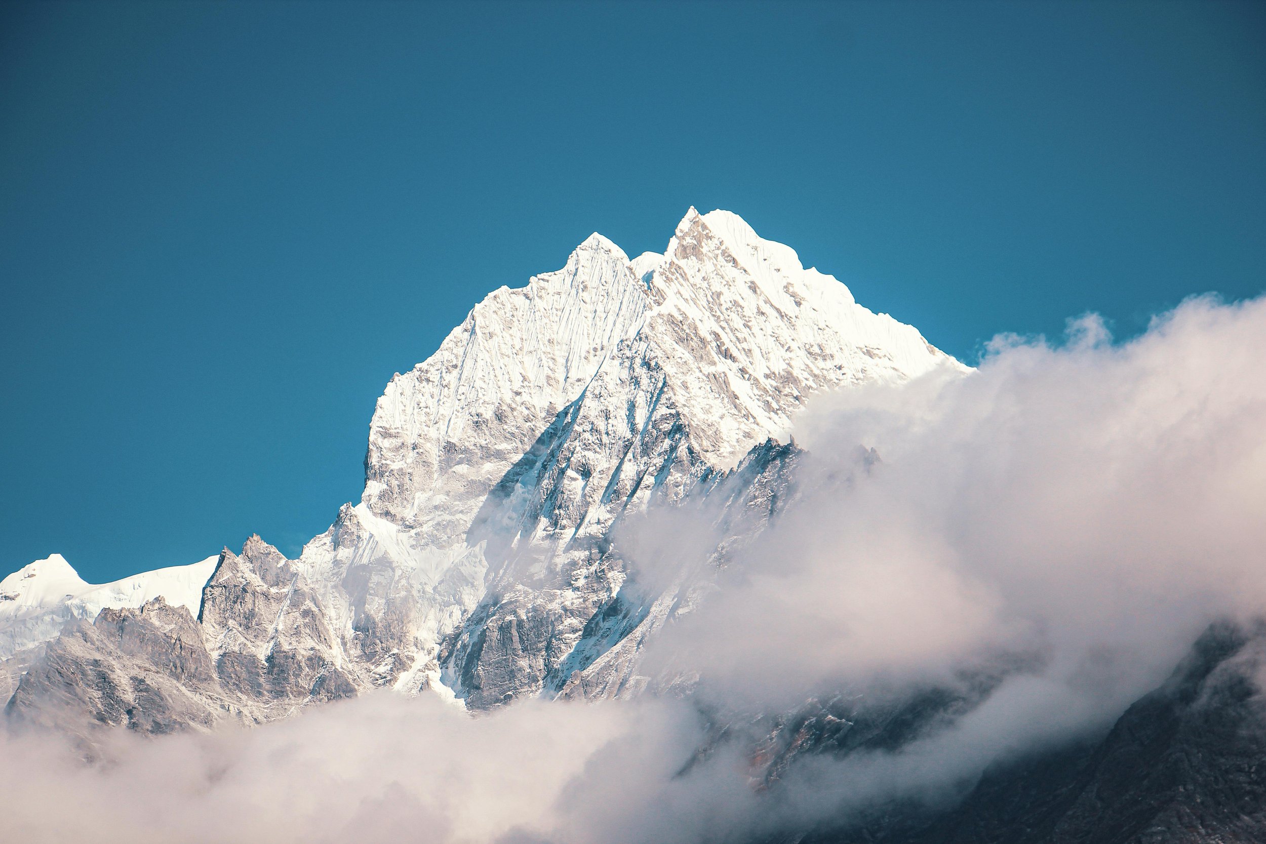 Snow-covered mountain peak rising above clouds against blue sky.