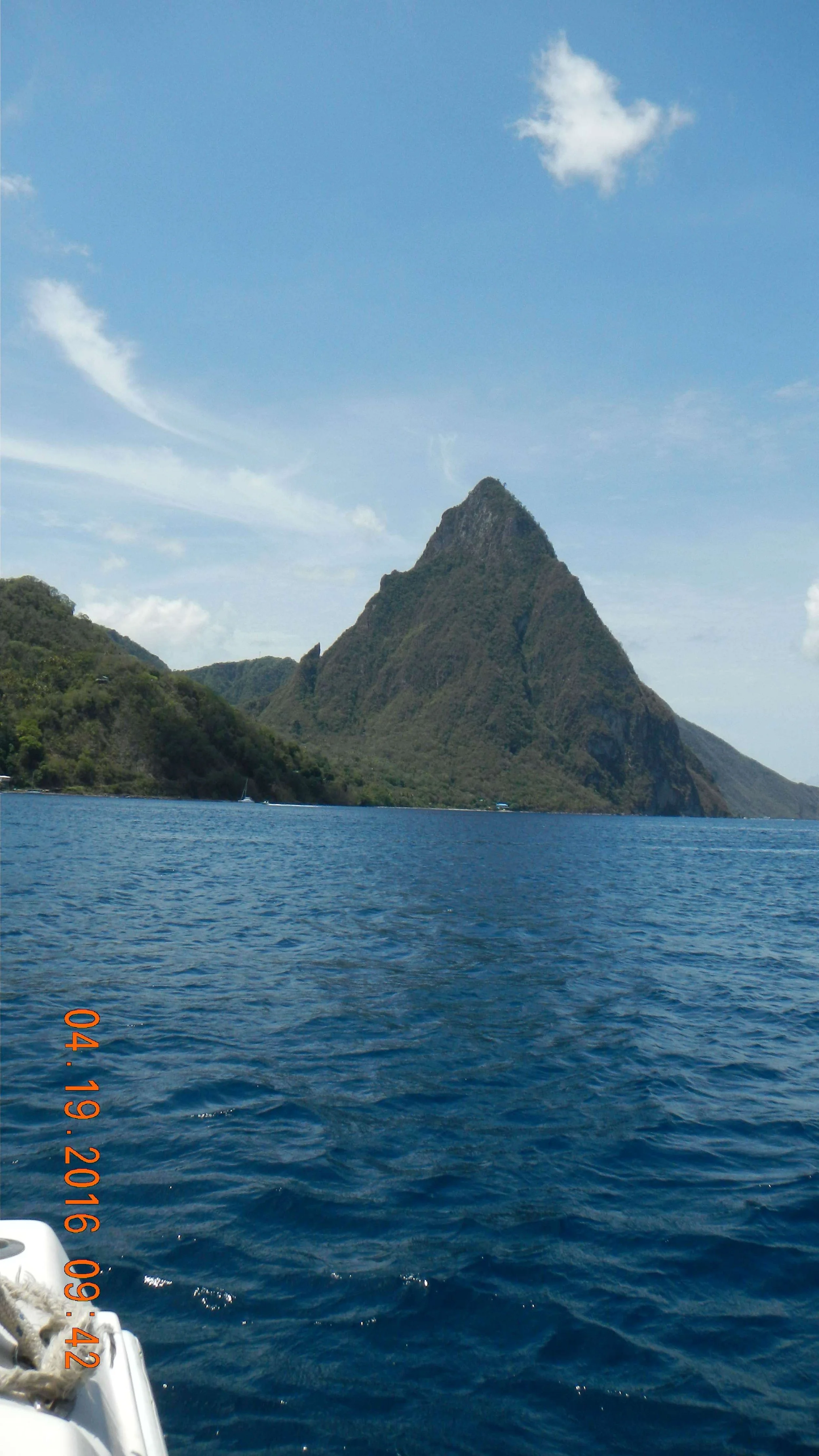 A view of the Pitons in St. Lucia, surrounded by blue water, under a partly cloudy sky.