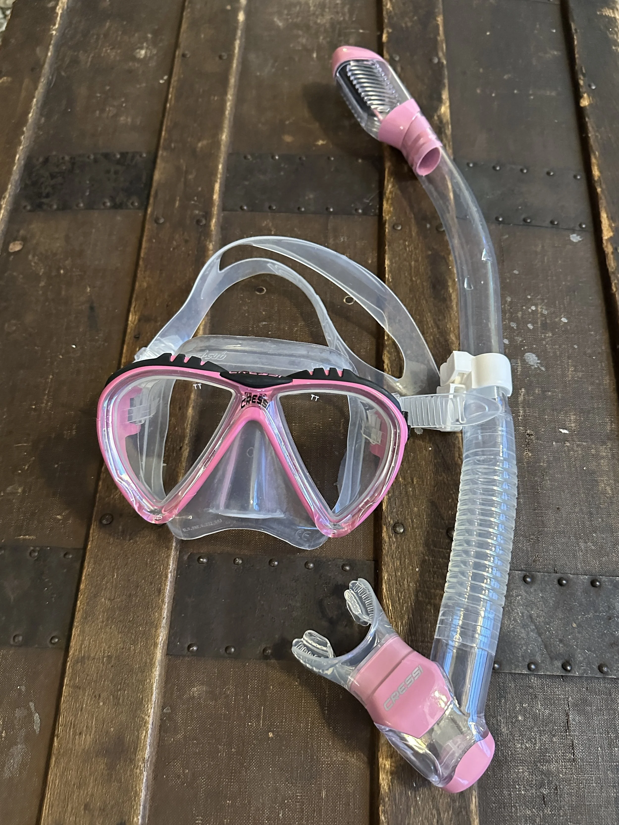 A pink and clear snorkeling mask and snorkel resting on a wooden surface.