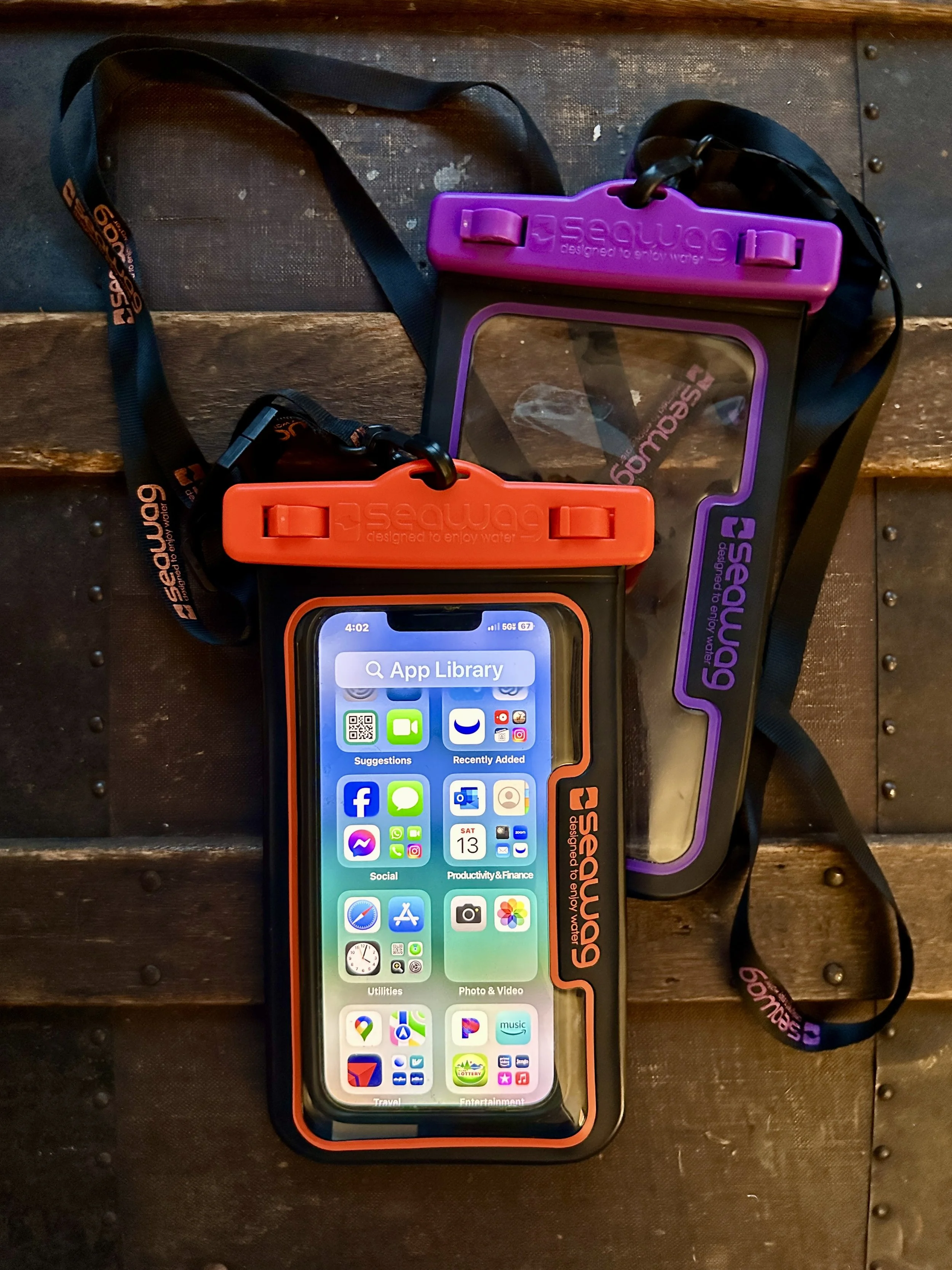 An iPhone with a protective case and waterproof pouch, both branded with 'SeaWing,' resting on a wooden surface.