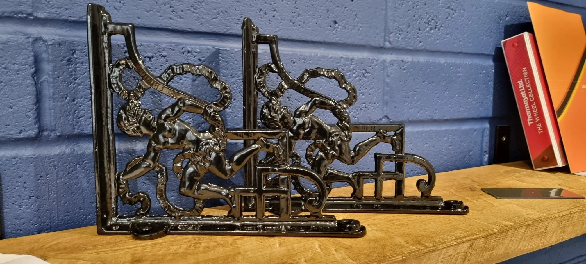 Decorative black metal horse sculptures on a wooden surface against a blue brick wall, with books or magazines nearby.