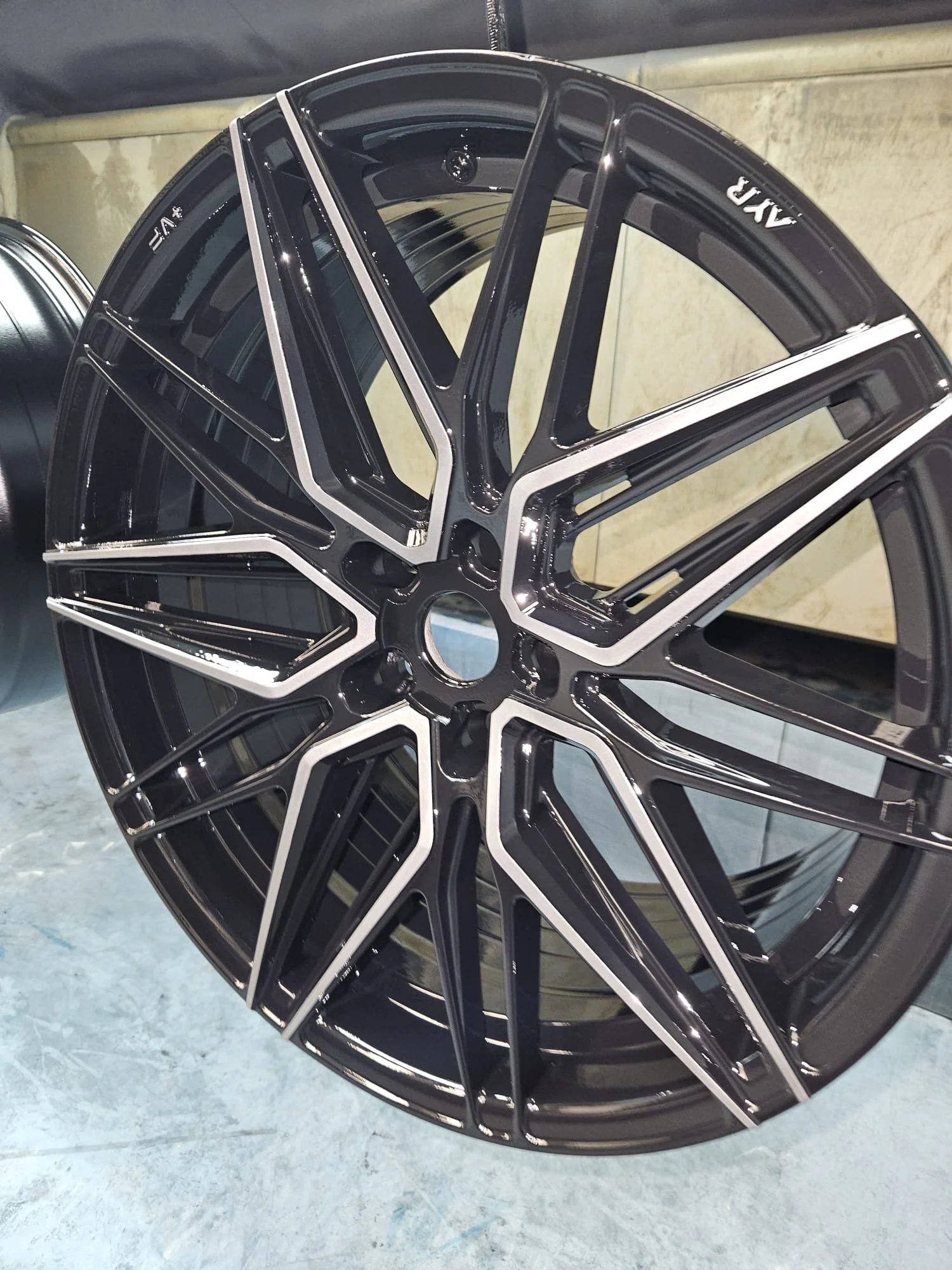Close-up of a black and silver multi-spoke alloy car wheel rim on a concrete floor.