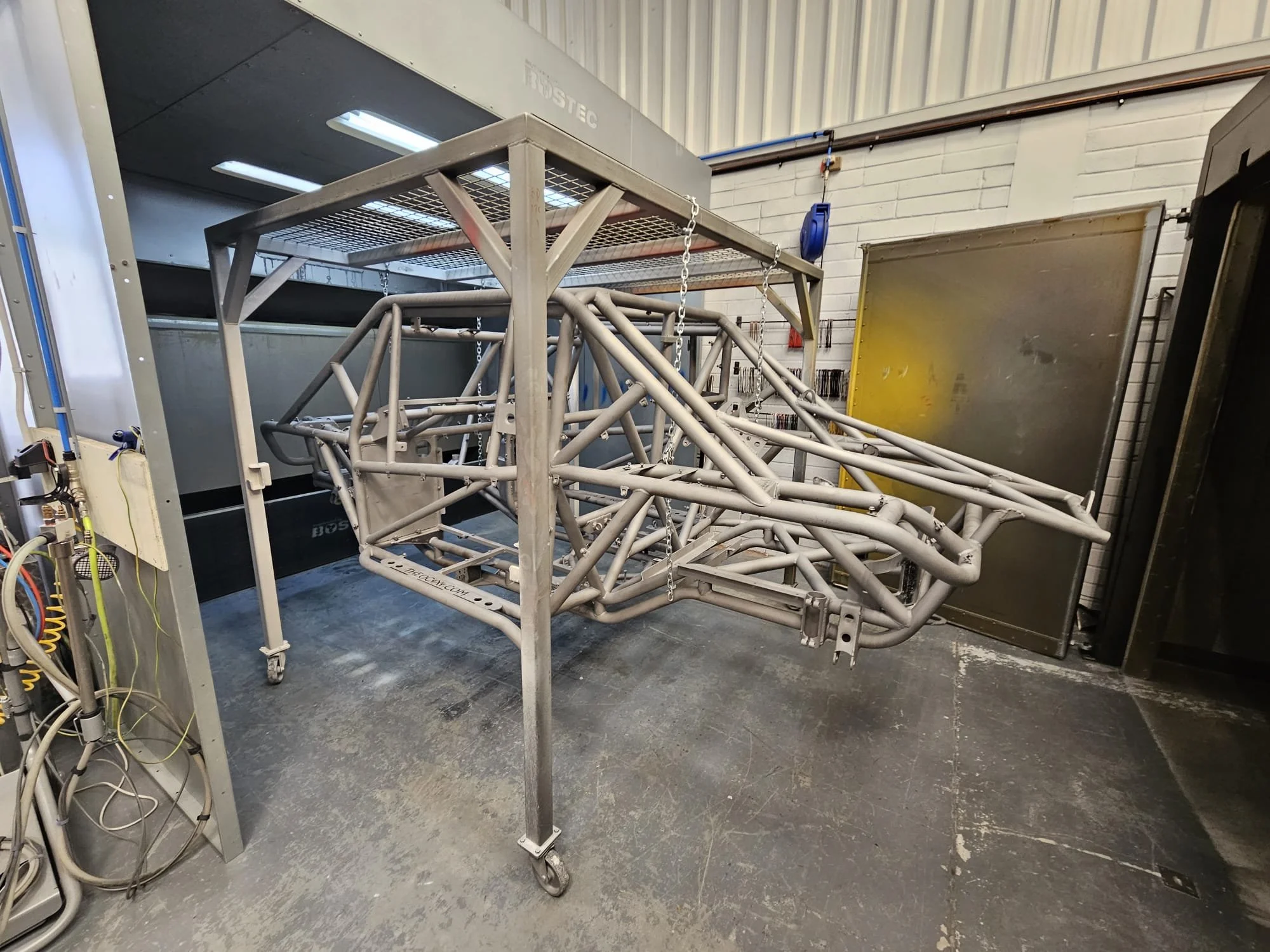 A metallic racing car chassis on a wheeled stand in a workshop.