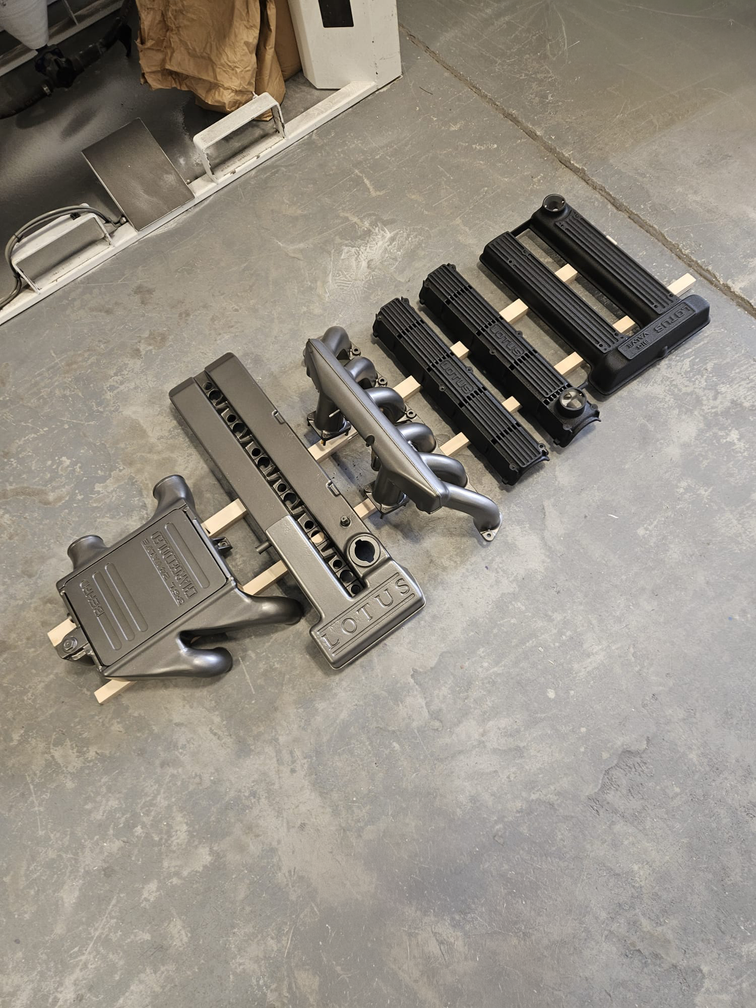 Four Lotus engine covers and valve covers placed on a concrete floor in a garage or workshop