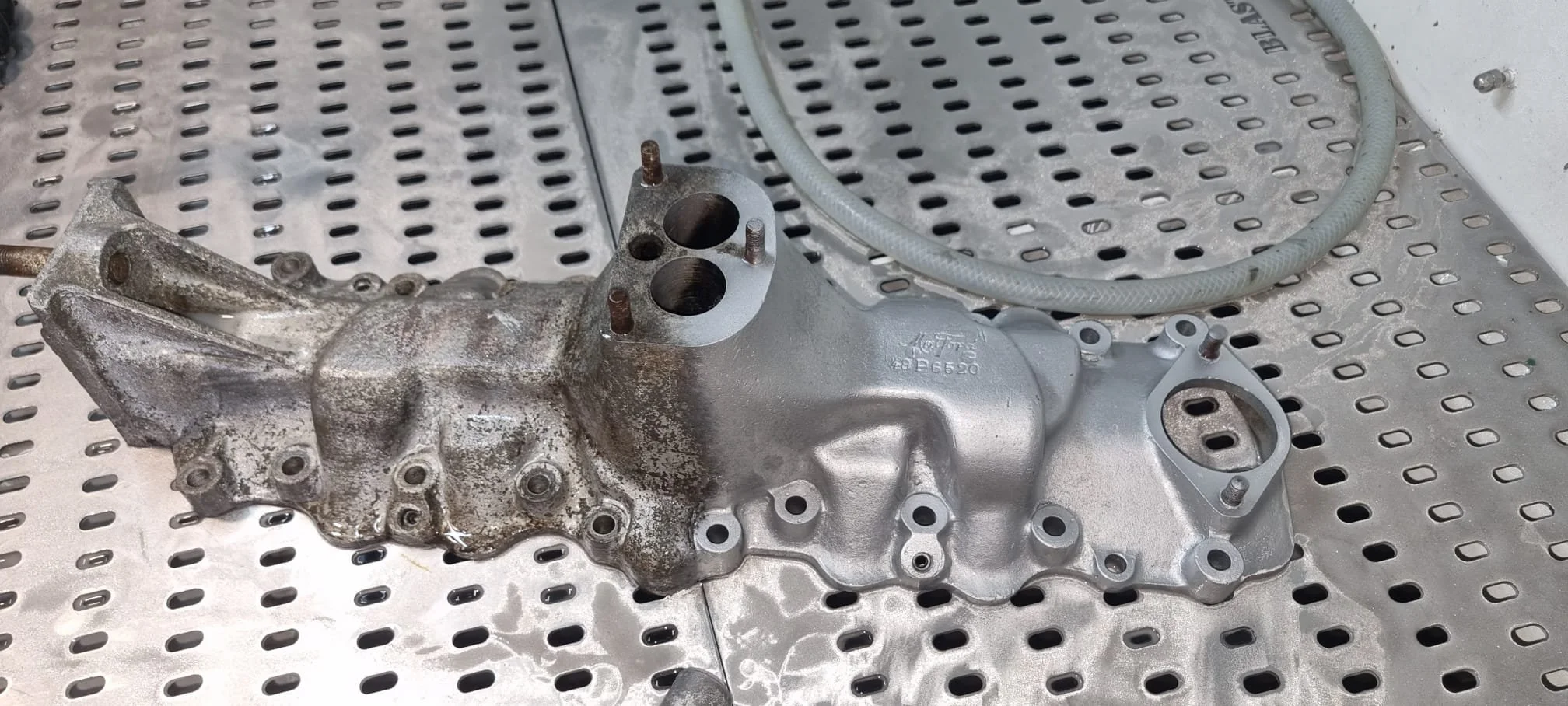 Metal engine component on perforated metal table with a gray hose nearby.