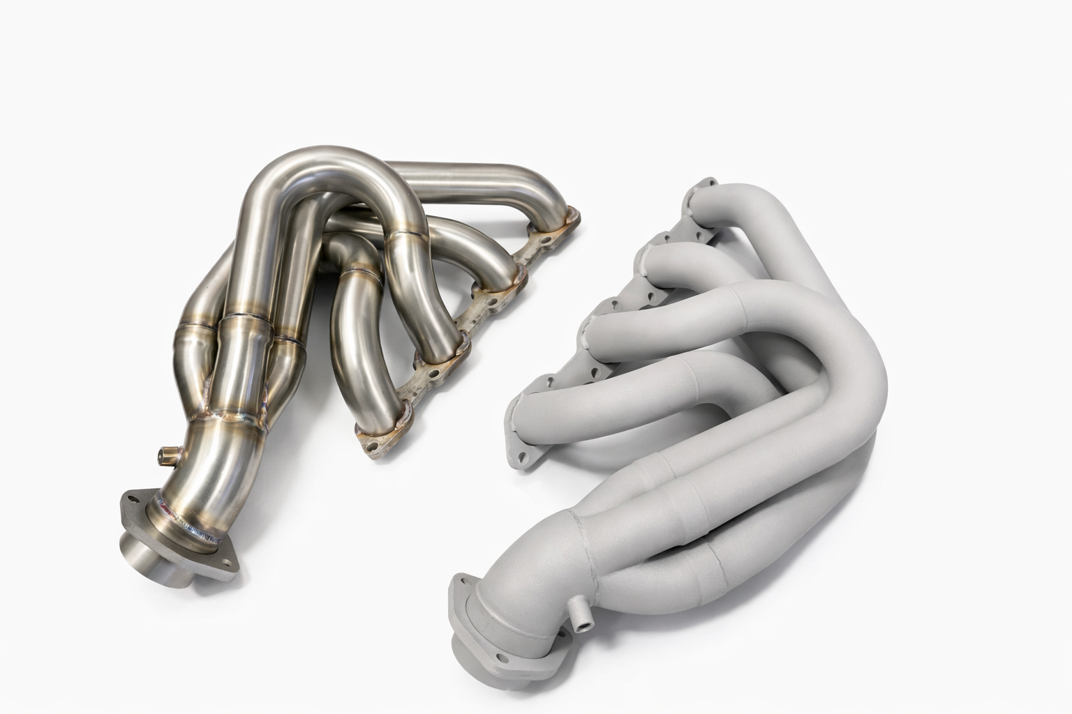 Two automotive exhaust headers, one metallic and shiny, the other has been blasted giving it a texture for painting, white background.