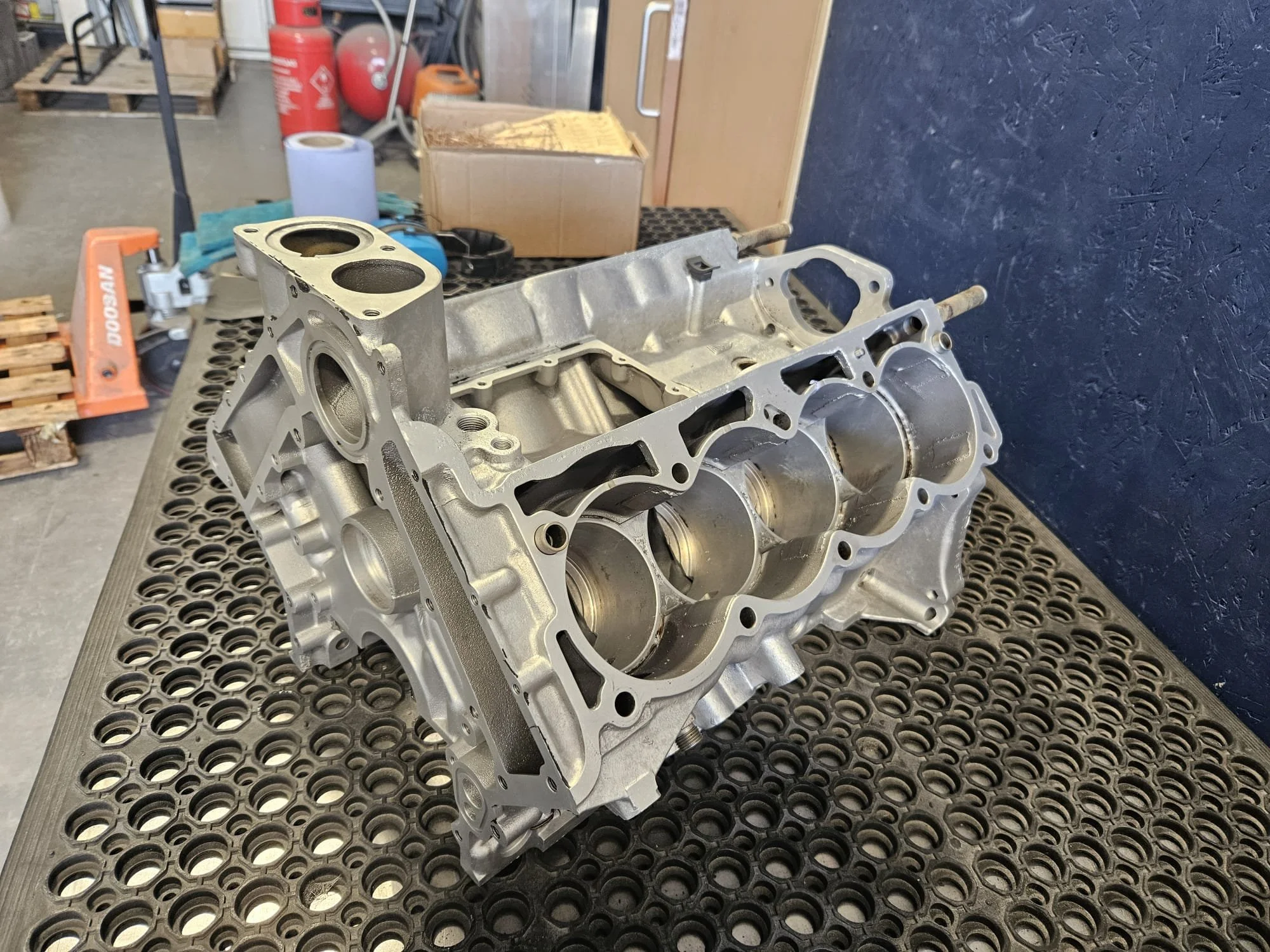 A silver car engine block resting on a black workbench in a workshop.