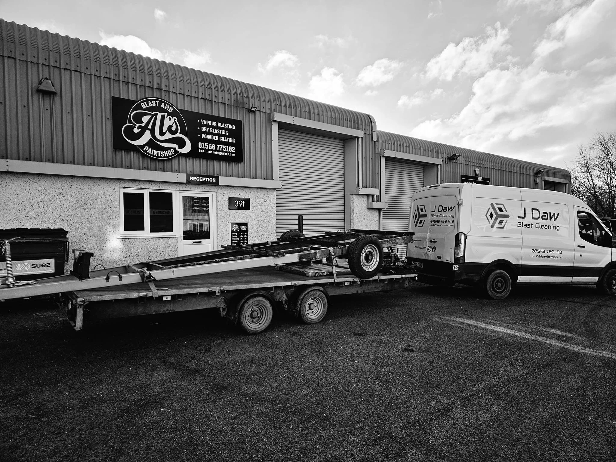 Exterior view of a paint shop with a pickup truck hauling a trailer and a van parked outside. The building has a sign for 'A's Paintshop' offering blast and paint services.