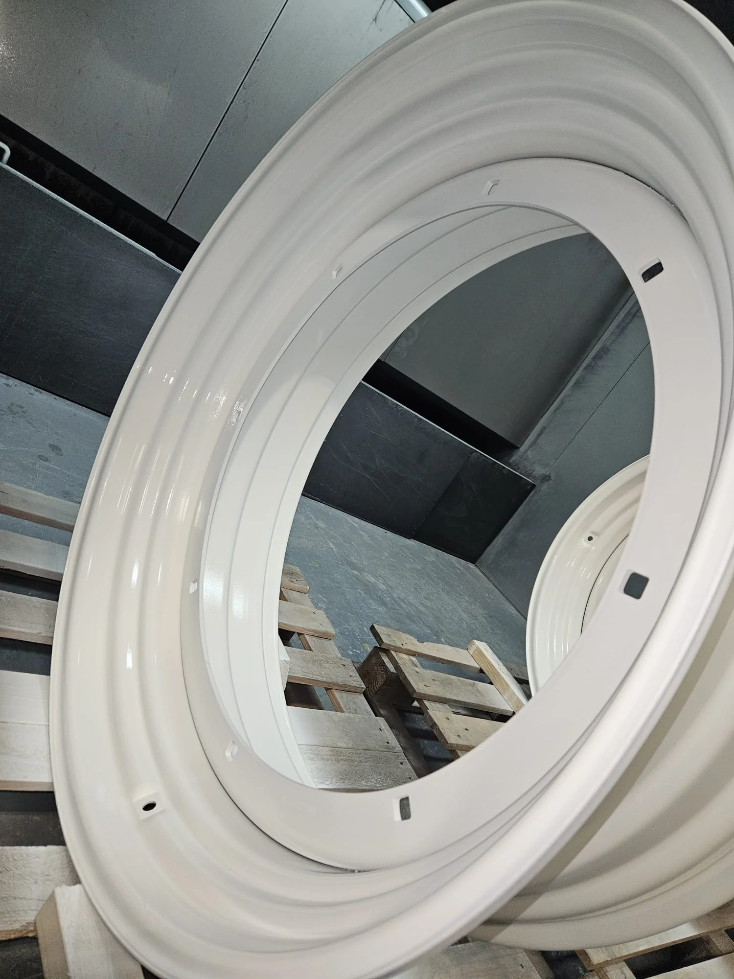Close-up of a disassembled white washing machine or dryer door frame, placed on a wooden pallet in a warehouse.