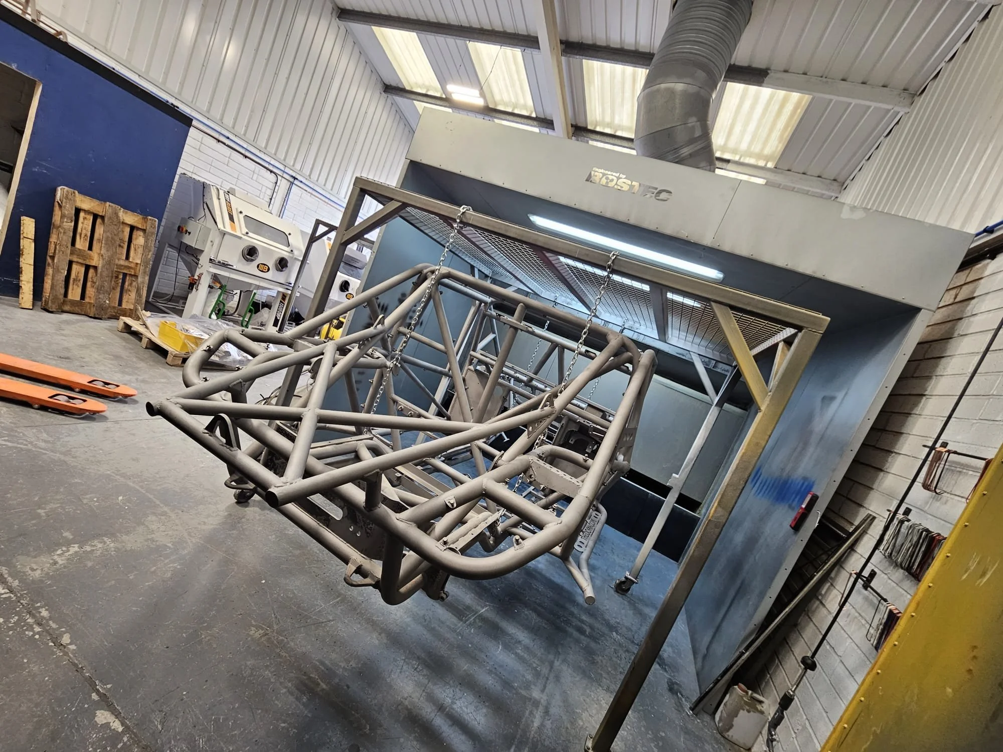 Metal car chassis frame inside a spray booth in a workshop.