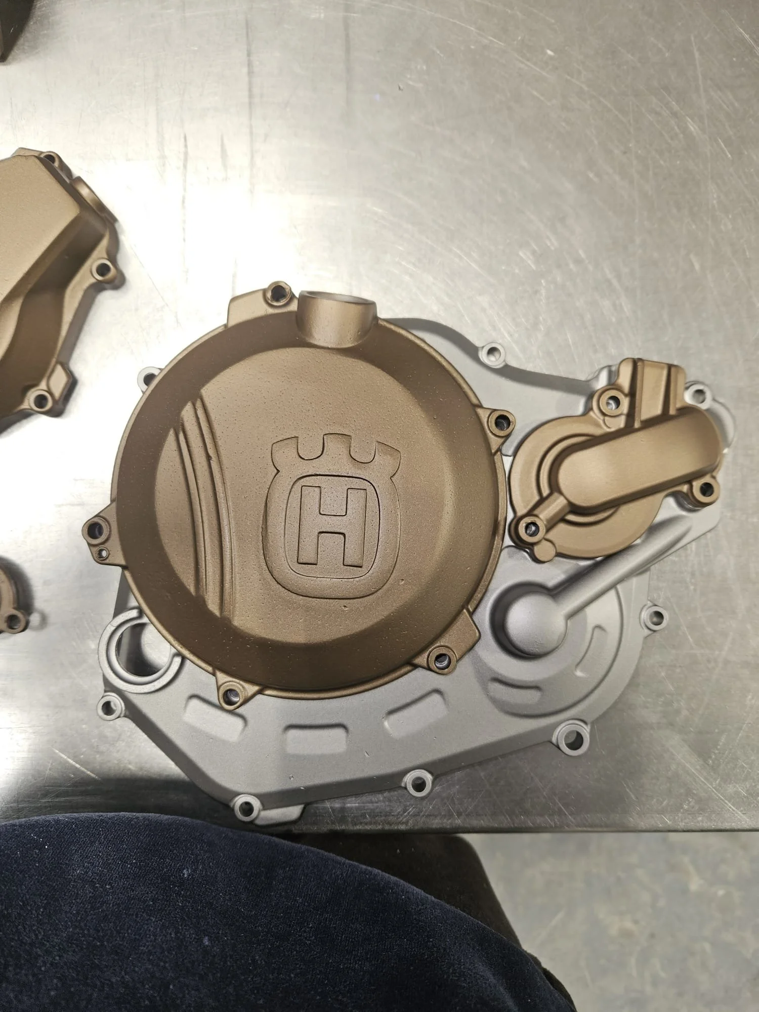 Close-up of a beige Honda engine cover freshly painted with a silver motorcycle engine housing underneath, on a metallic surface.