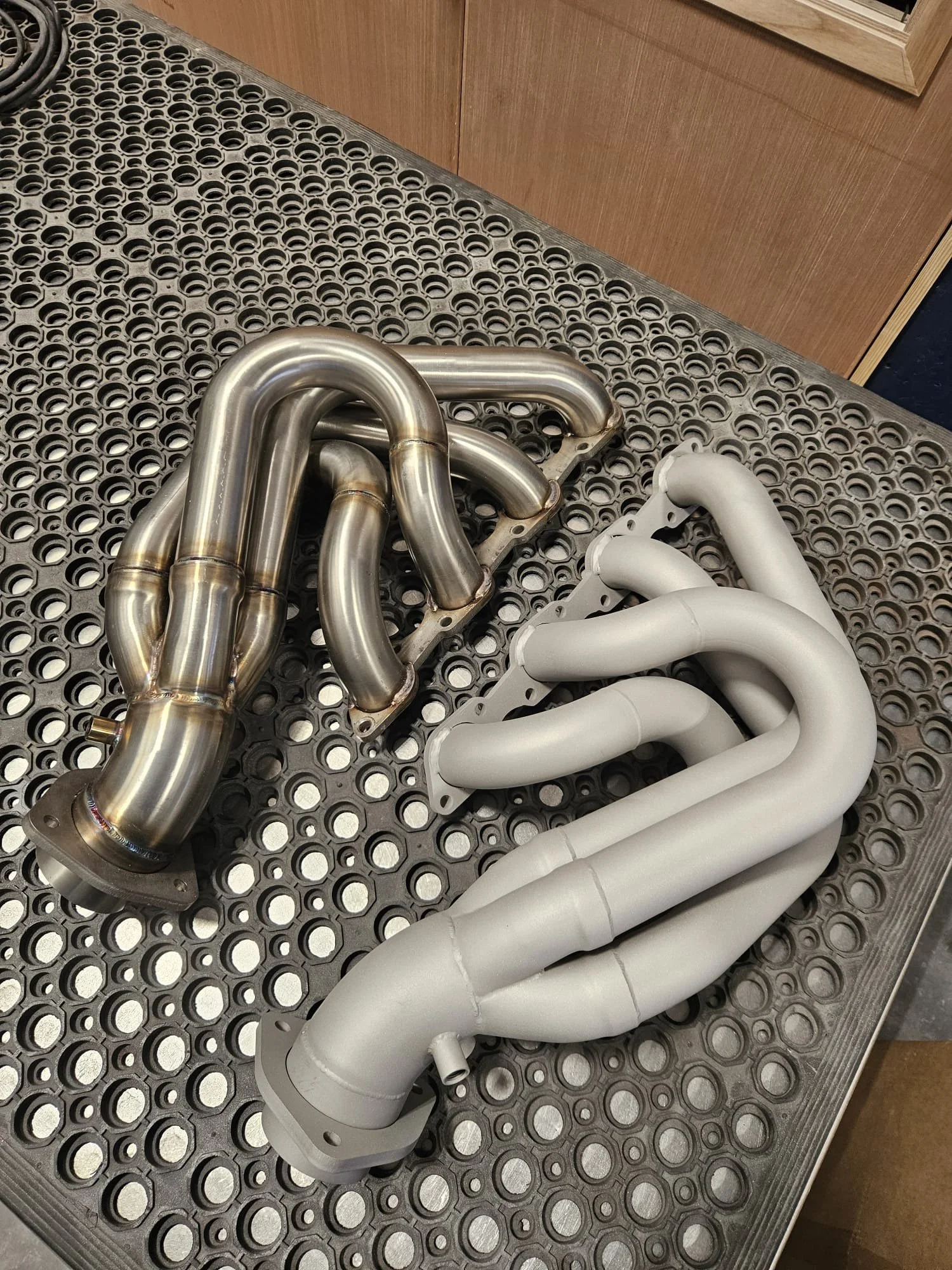 Metal automotive exhaust headers on a perforated metal surface before and after blasting.