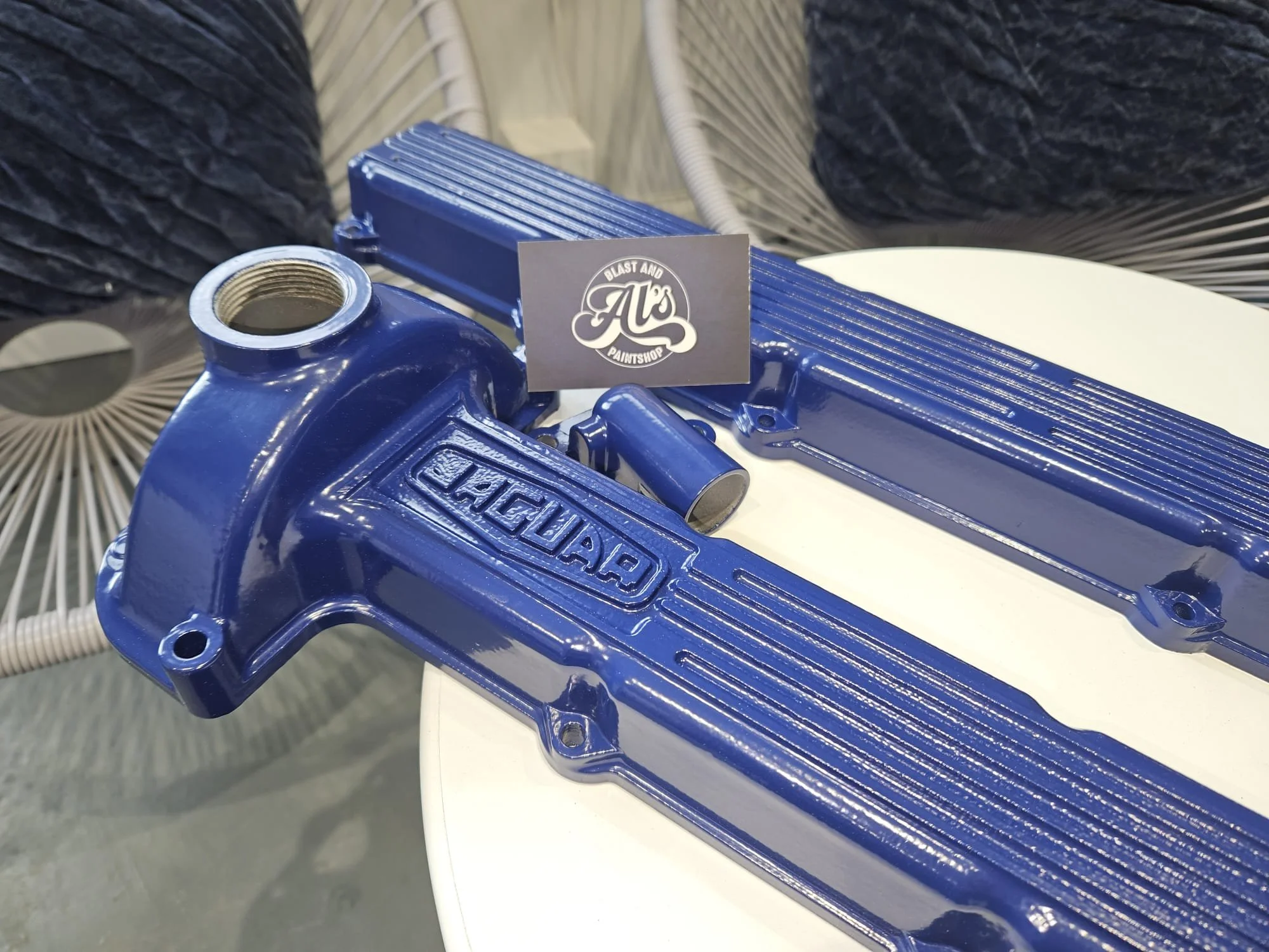 Blue jaguar engine valve covers and intake manifold freshly painted on display at a paint shop, with a logo sign. The valve covers have 'jaguar' embossed on them.