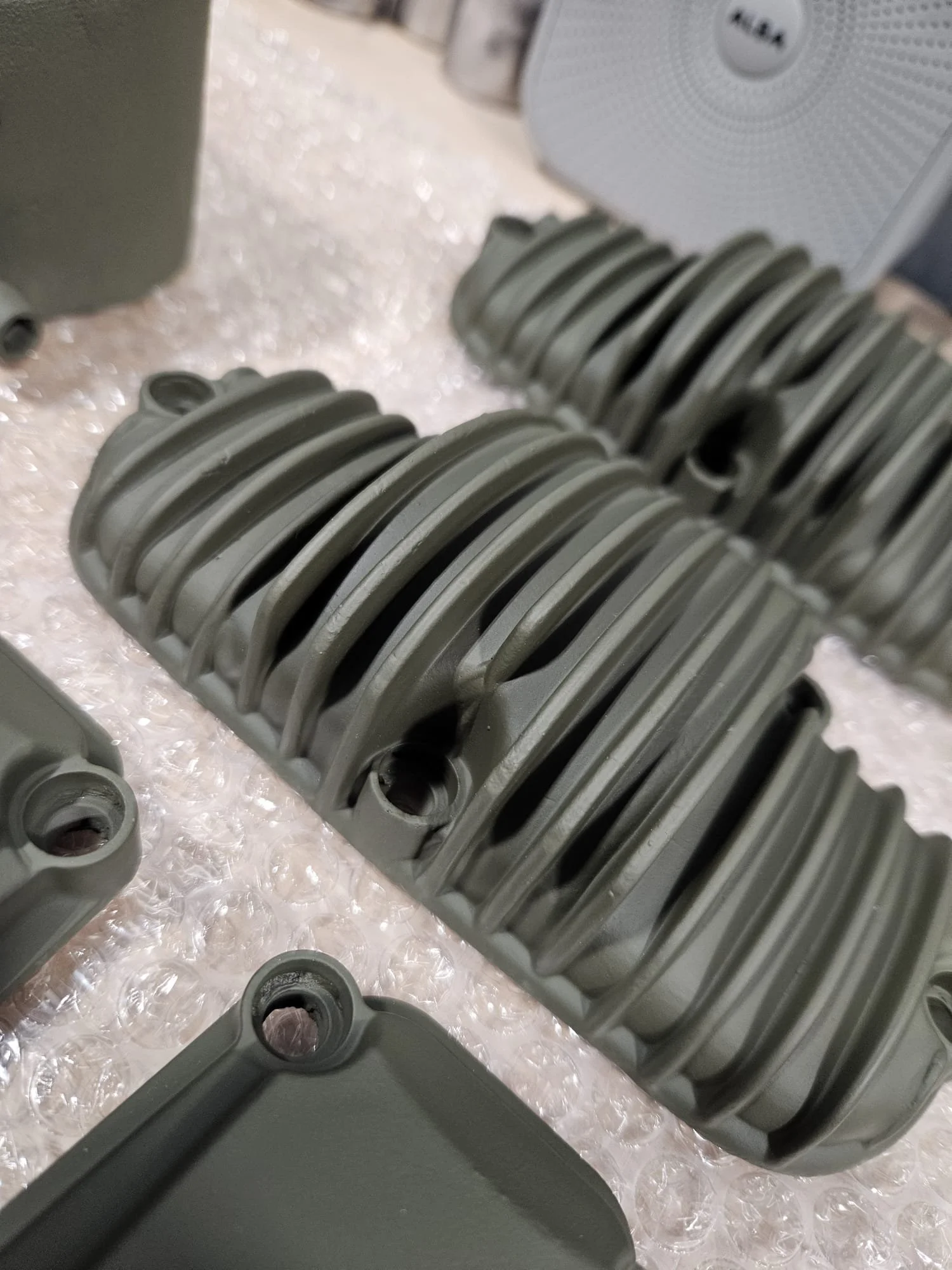 Close-up of gray metal engine cylinder heads with fins, placed on bubble wrap, with electronic equipment in background.