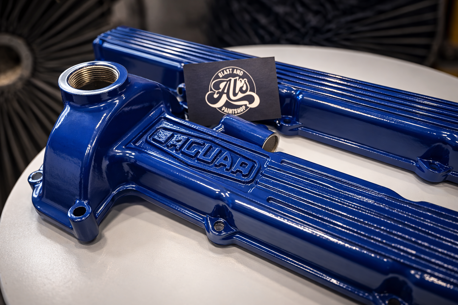 Blue Jaguar valve covers displayed on a white surface with a black business card reading 'Al's Blast and Paintshop' in the background.