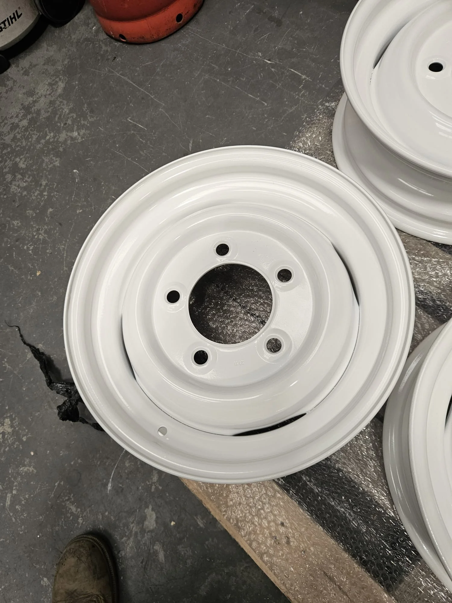 Several white metal wheels with a central hole and four smaller holes are stacked on a workbench.