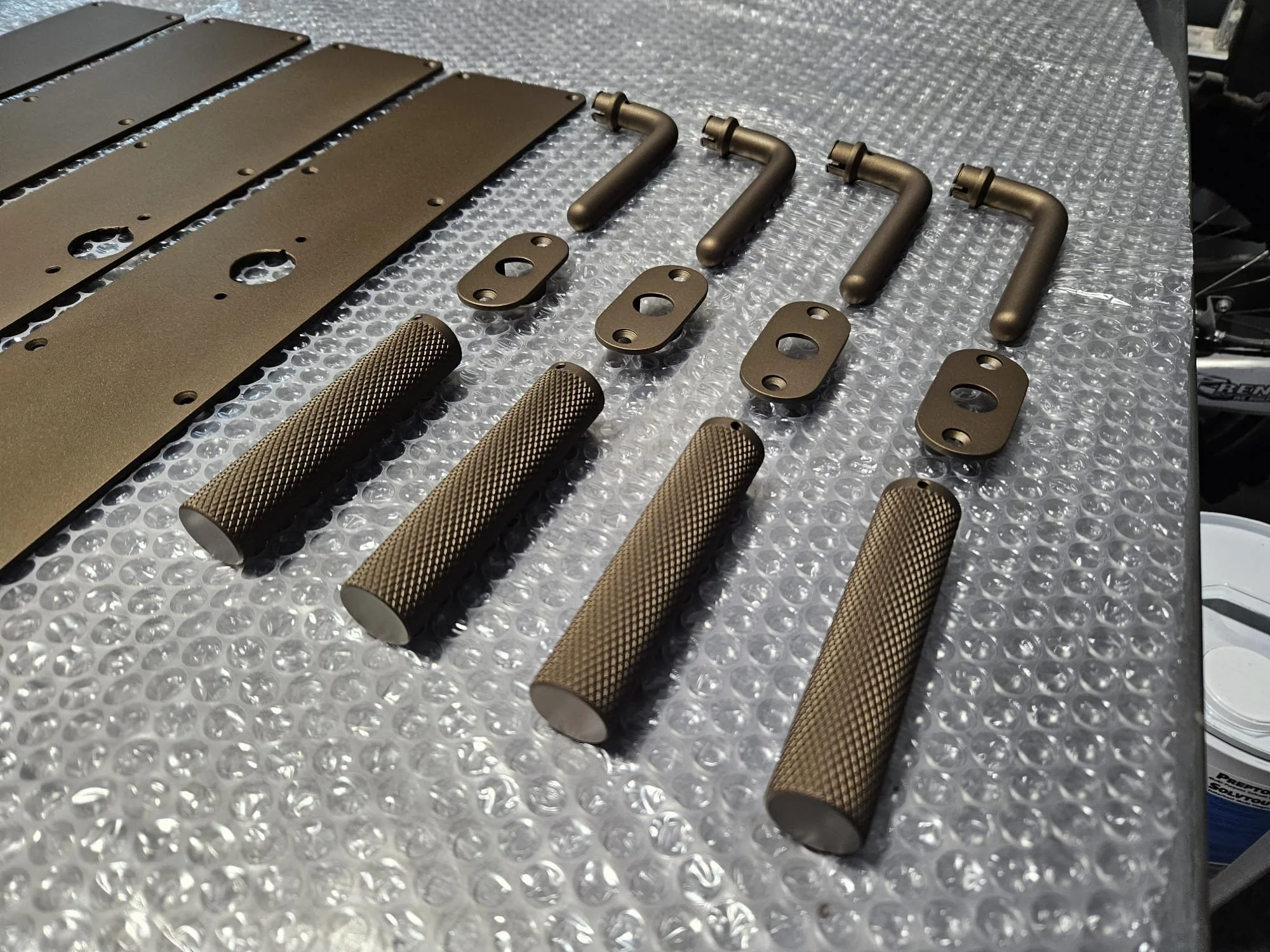 Various metal cerakote finished door handles and door parts, arranged on a bubble wrap surface.
