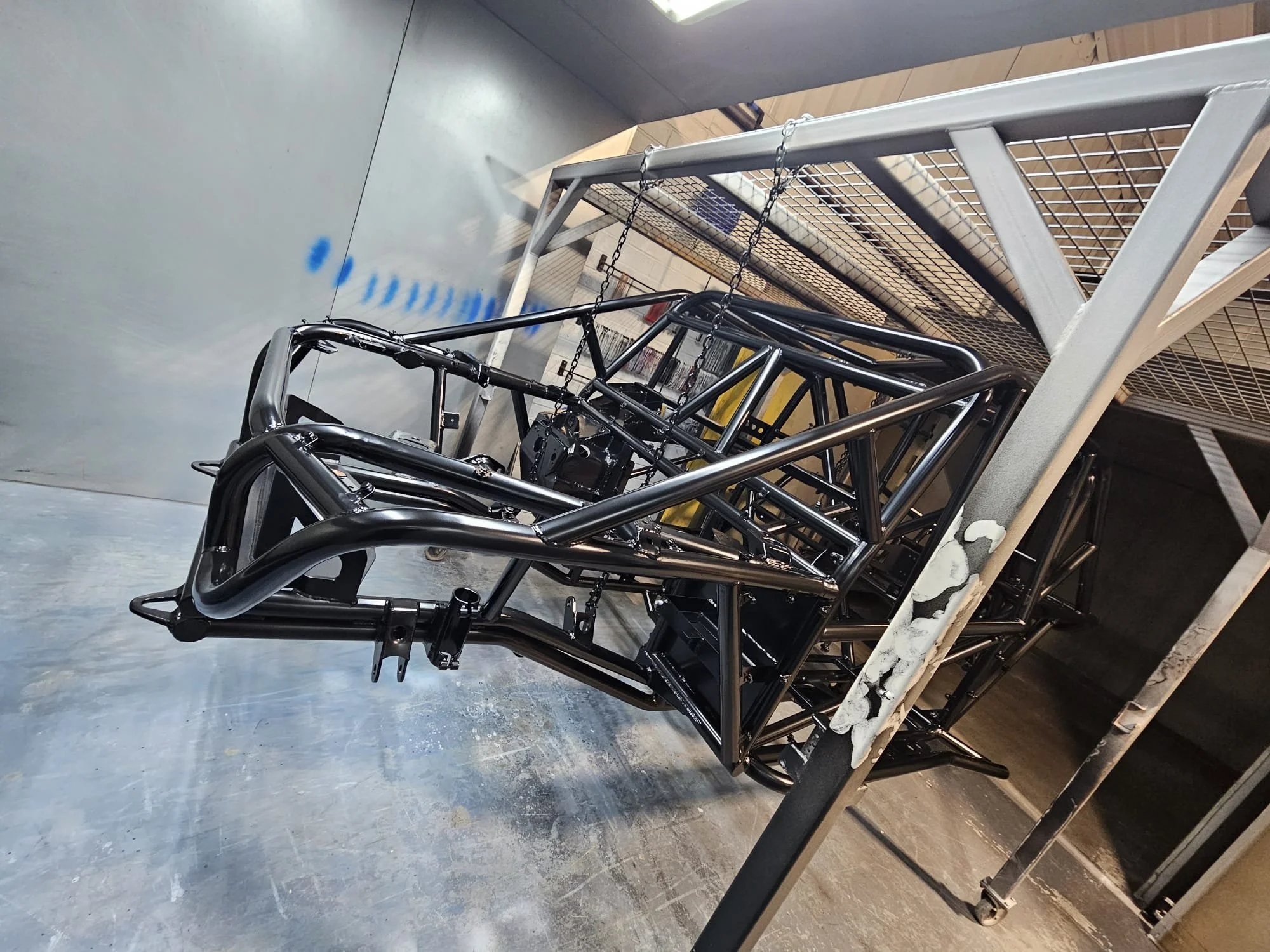 Black powder coated metal roll cage frame for a race car on a metal cart inside a workshop