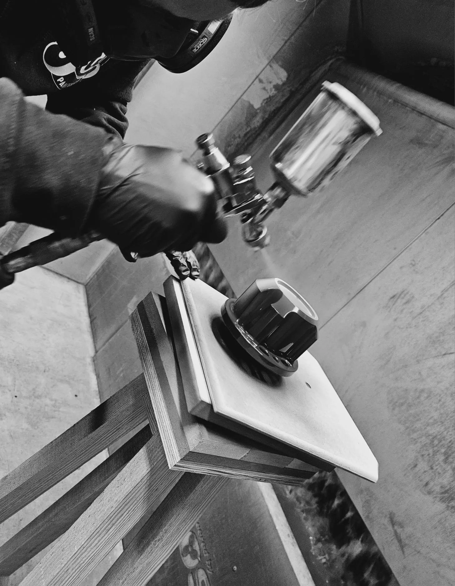 A person wearing gloves holding a spray gun, painting a wooden table top in black and white.