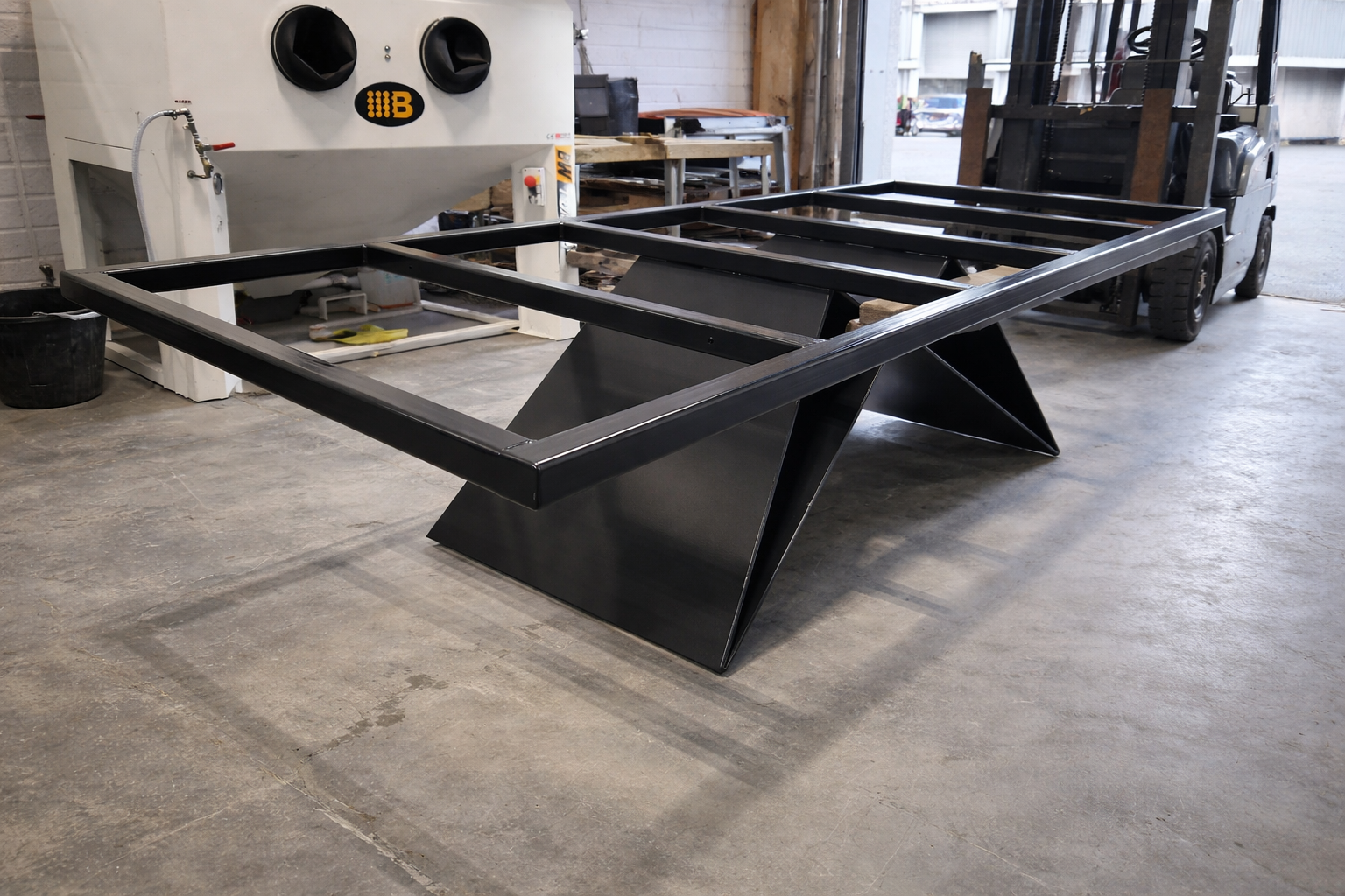 Metal table frame structure in a workshop, with a black powder coated finish, likely a furniture or equipment component.