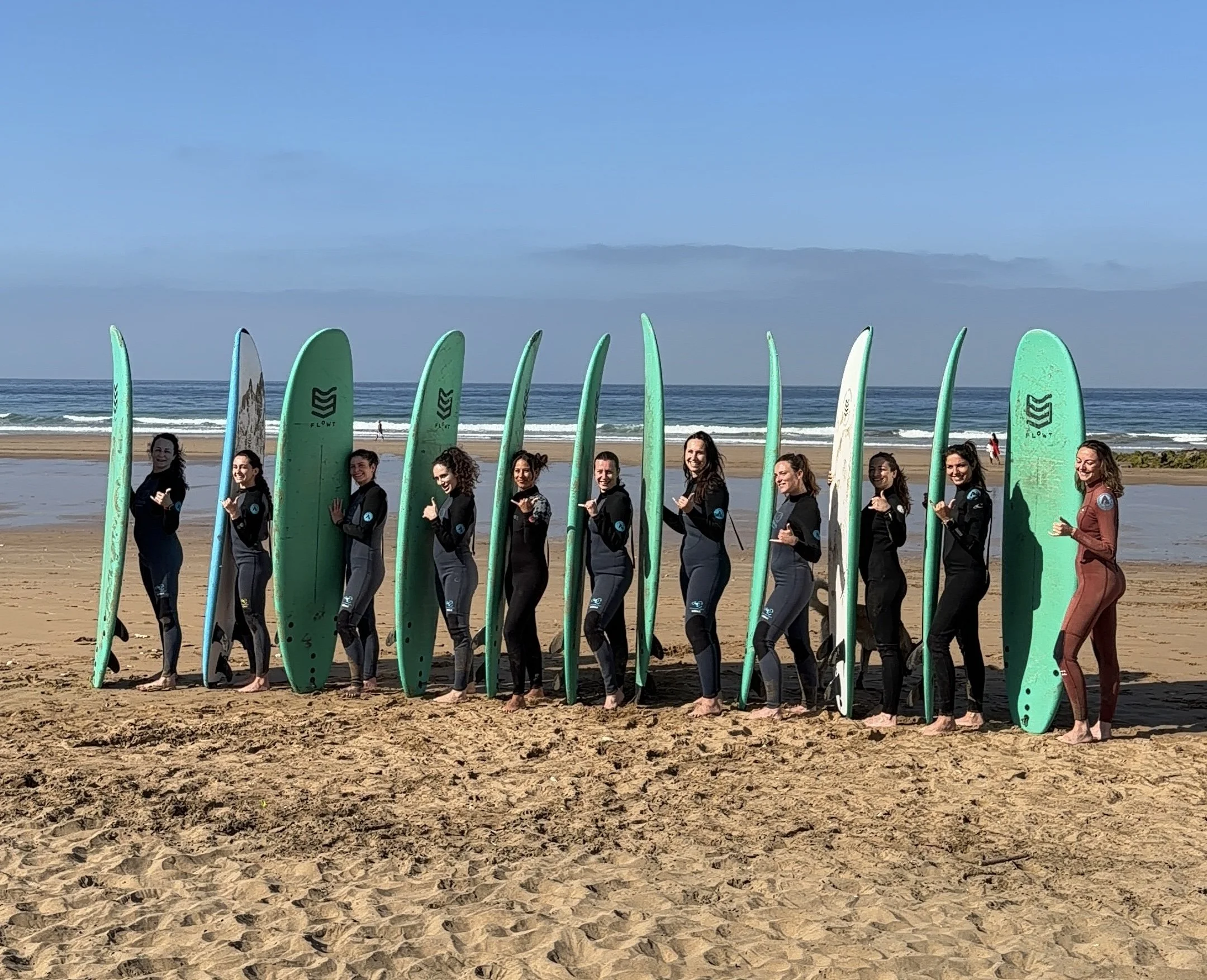 Un groupe de personnes en combinaison de surf posant avec leurs planches de surf sur la plage.