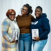 Three women standing happily together, holding papers and smiling at the camera.