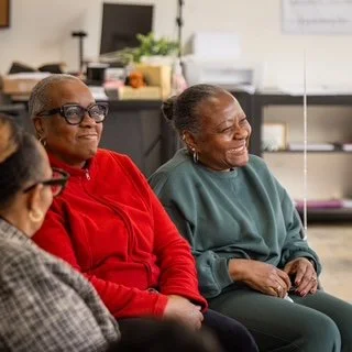 Three elderly women sitting together and smiling in a comfortable room.