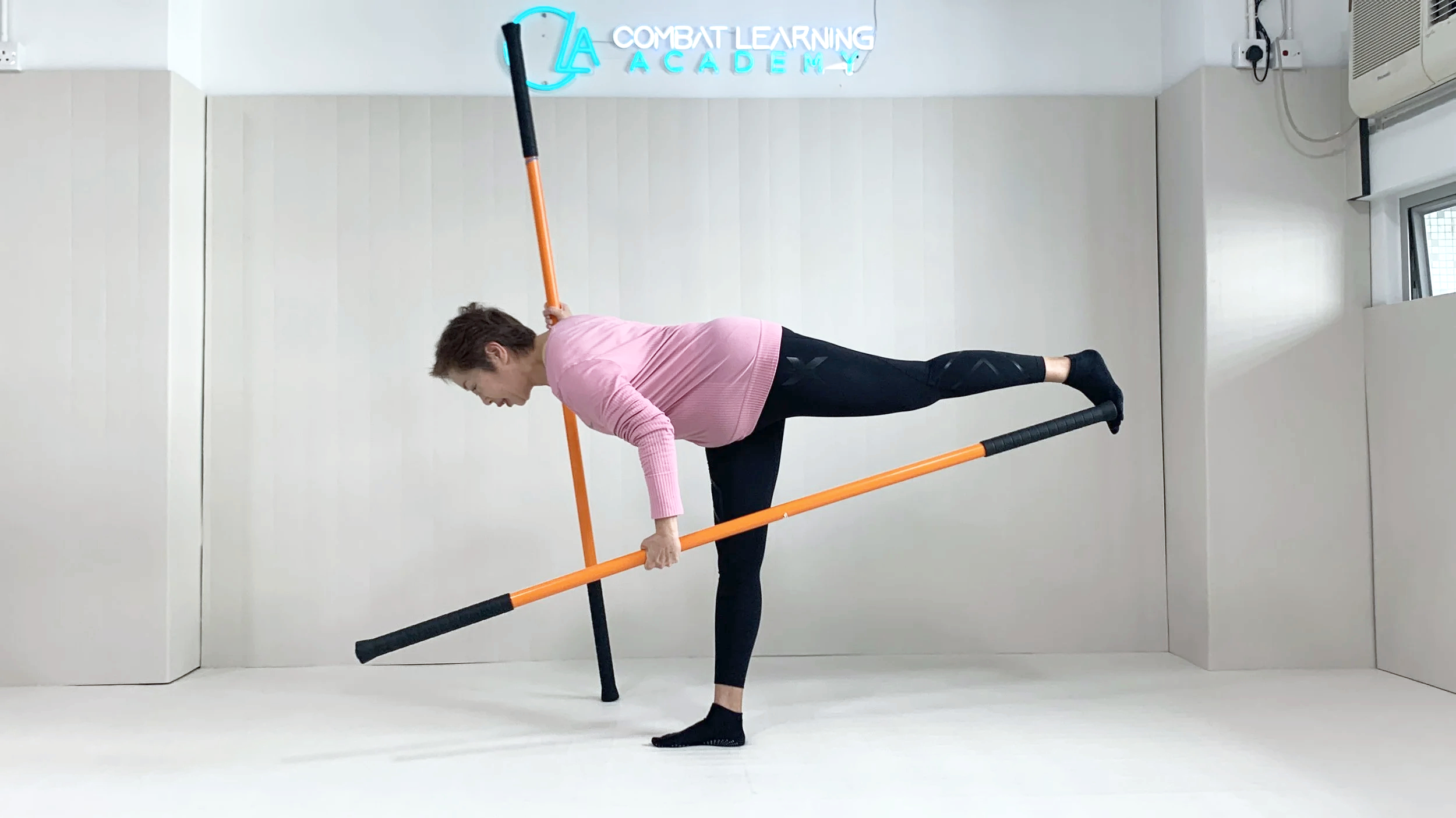 Person in pink shirt and black leggings practicing movement & mobility  with a mobility stick.